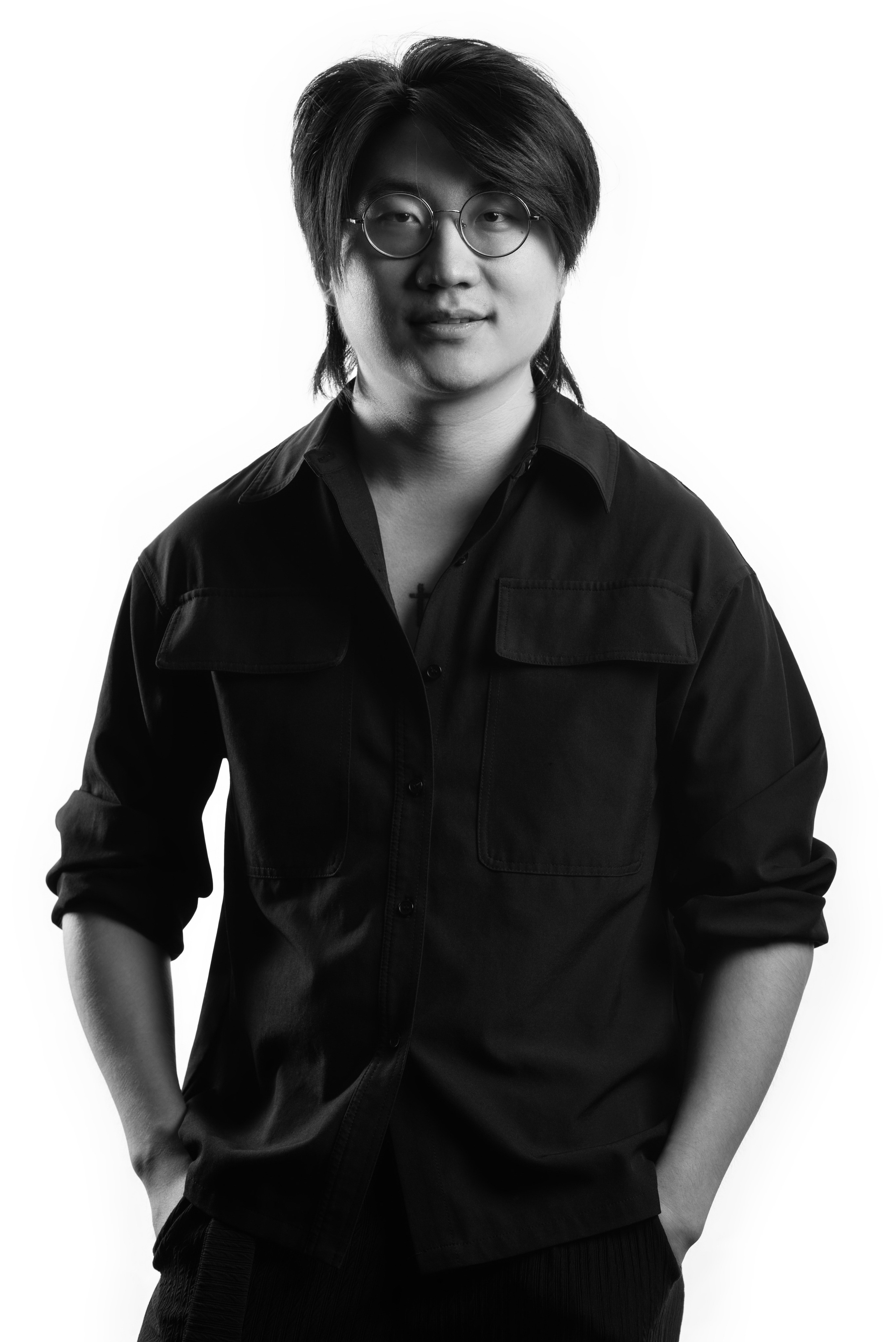 A black-and-white corporate portrait featuring a smiling young man with short hair and glasses, wearing a casual hoodie with a minimal graphic design. Photographed against a crisp white background, the image captures a relaxed yet professional vibe, ideal for modern corporate teams in Singapore looking for approachable and authentic portrait photography.