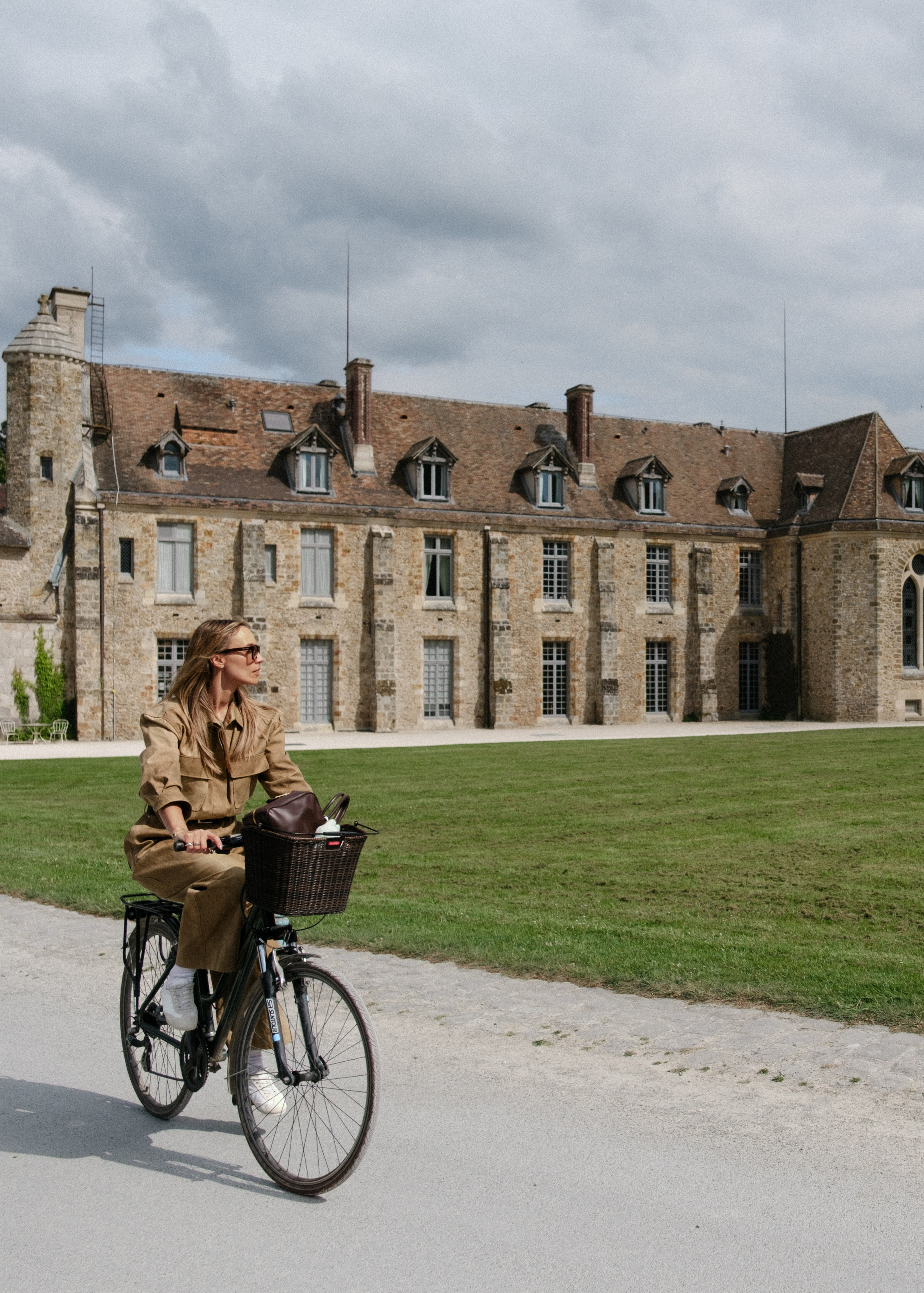 Commercial lookbook look with a khaki boilersuit on a bicycle near a French chateau