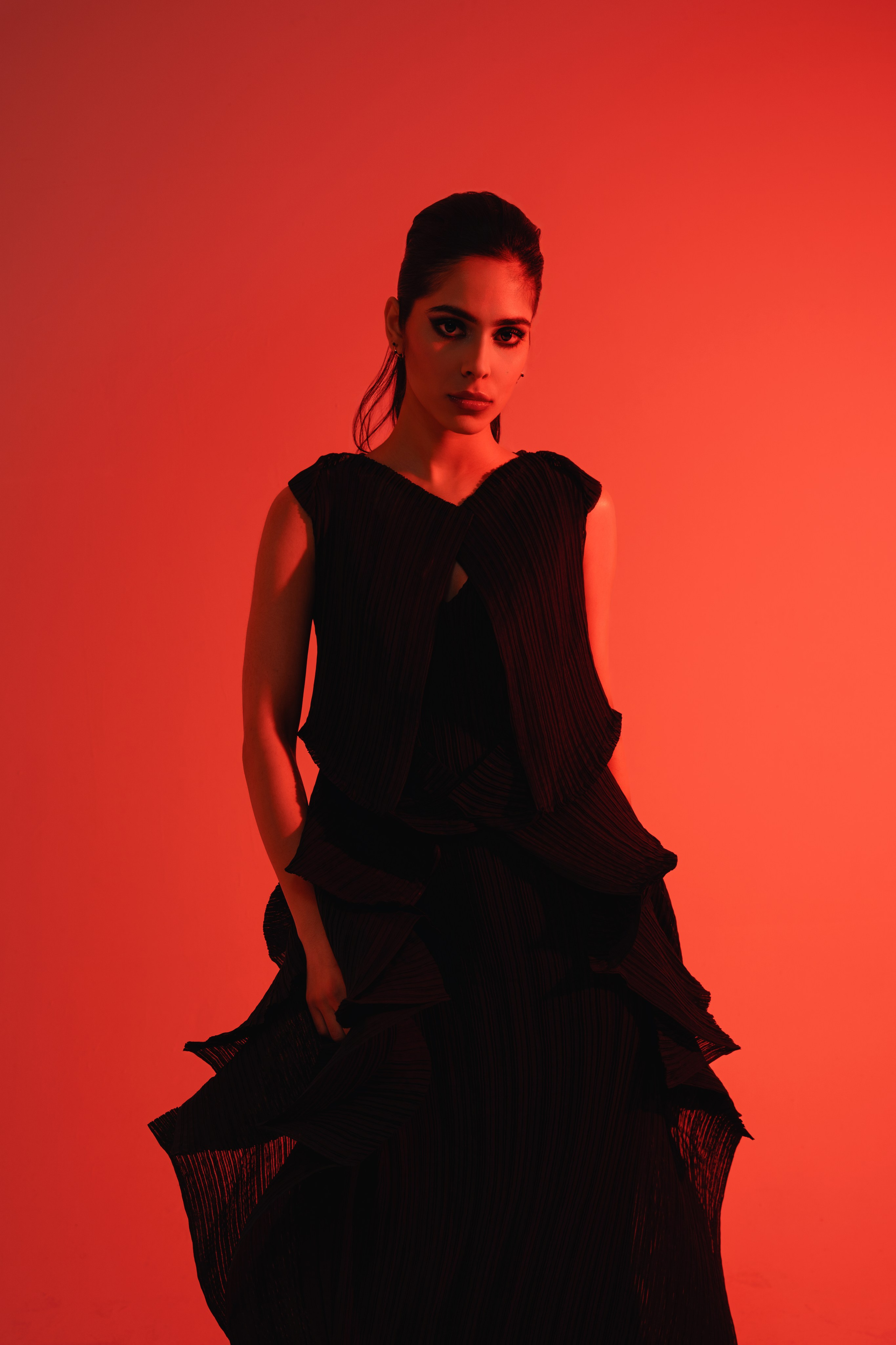 Futuristic Fashion Photography with Red Lighting – A model striking a dynamic pose in a black outfit from Issey Miyake, captured in a modern fashion shoot using blue lighting to create an edgy, contemporary atmosphere