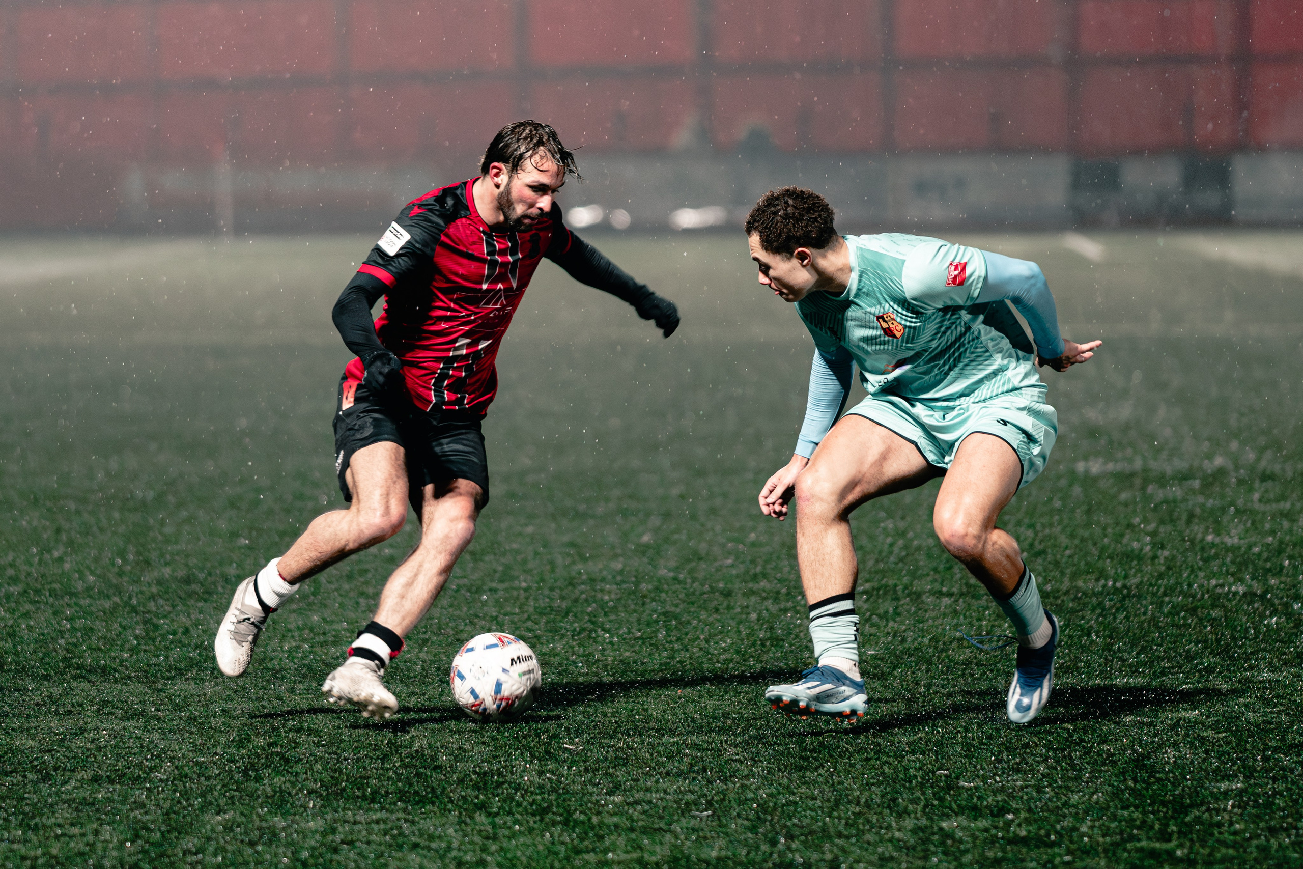 Tyler Roberts dribbles in heavy rain as Ethan Sephton closes him down during the Birmingham Senior Cup match between Tamworth FC and Alvechurch at The Lamb Ground, Feb 3 2026.