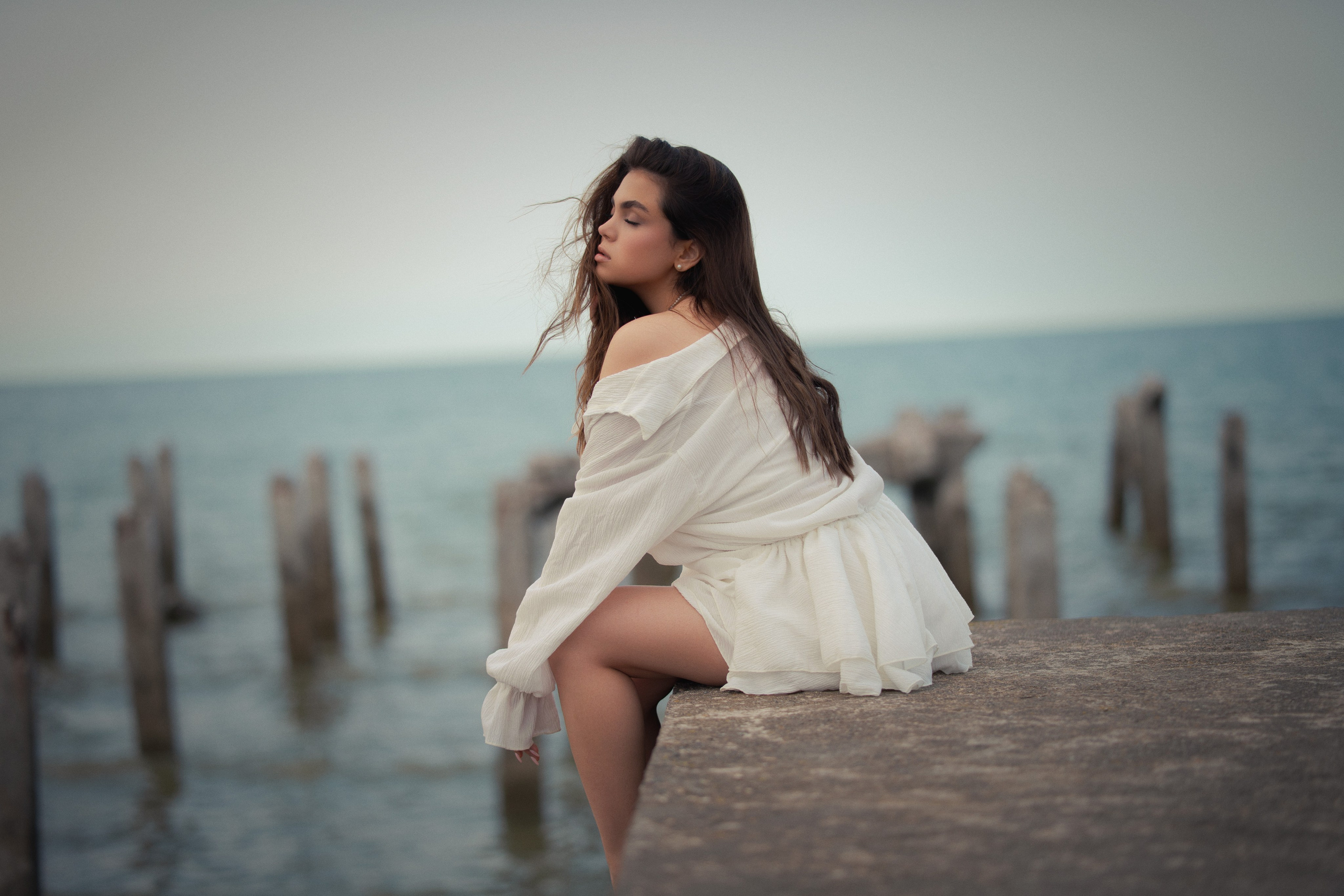 Fine art female portrait photography by Mehran Hadad featuring a young woman sitting on a pier with ocean scenery and cinematic natural lighting.