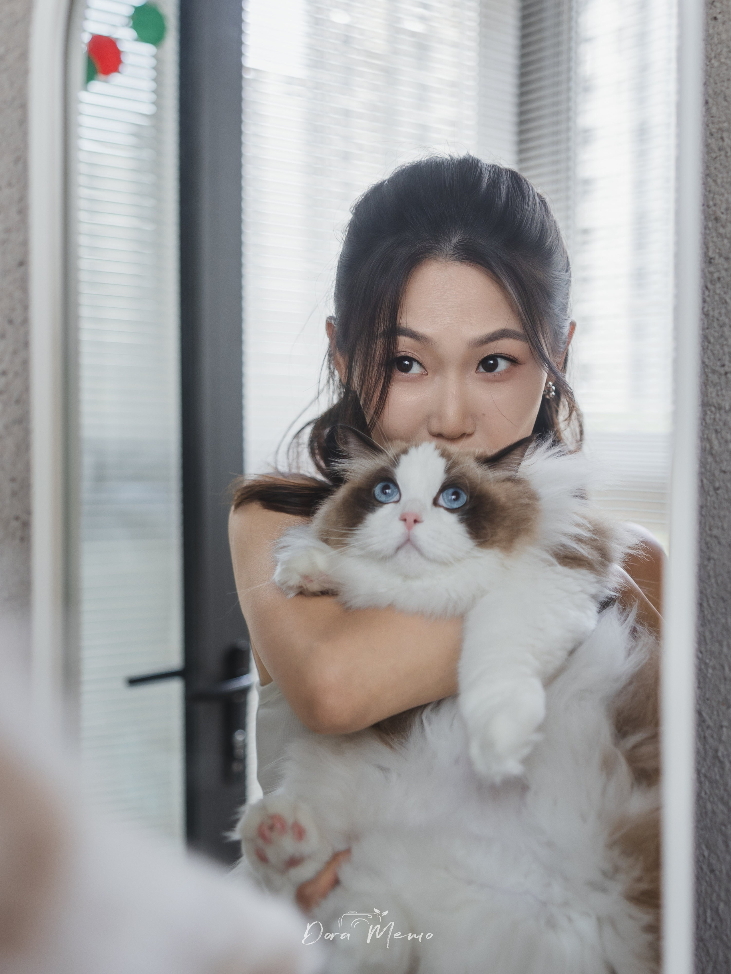 A woman holds her fluffy ragdoll cat in front of a mirror, her eyes peeking over the cat’s head — a cozy, heartfelt portrait from a Shanghai pet and home photography session.