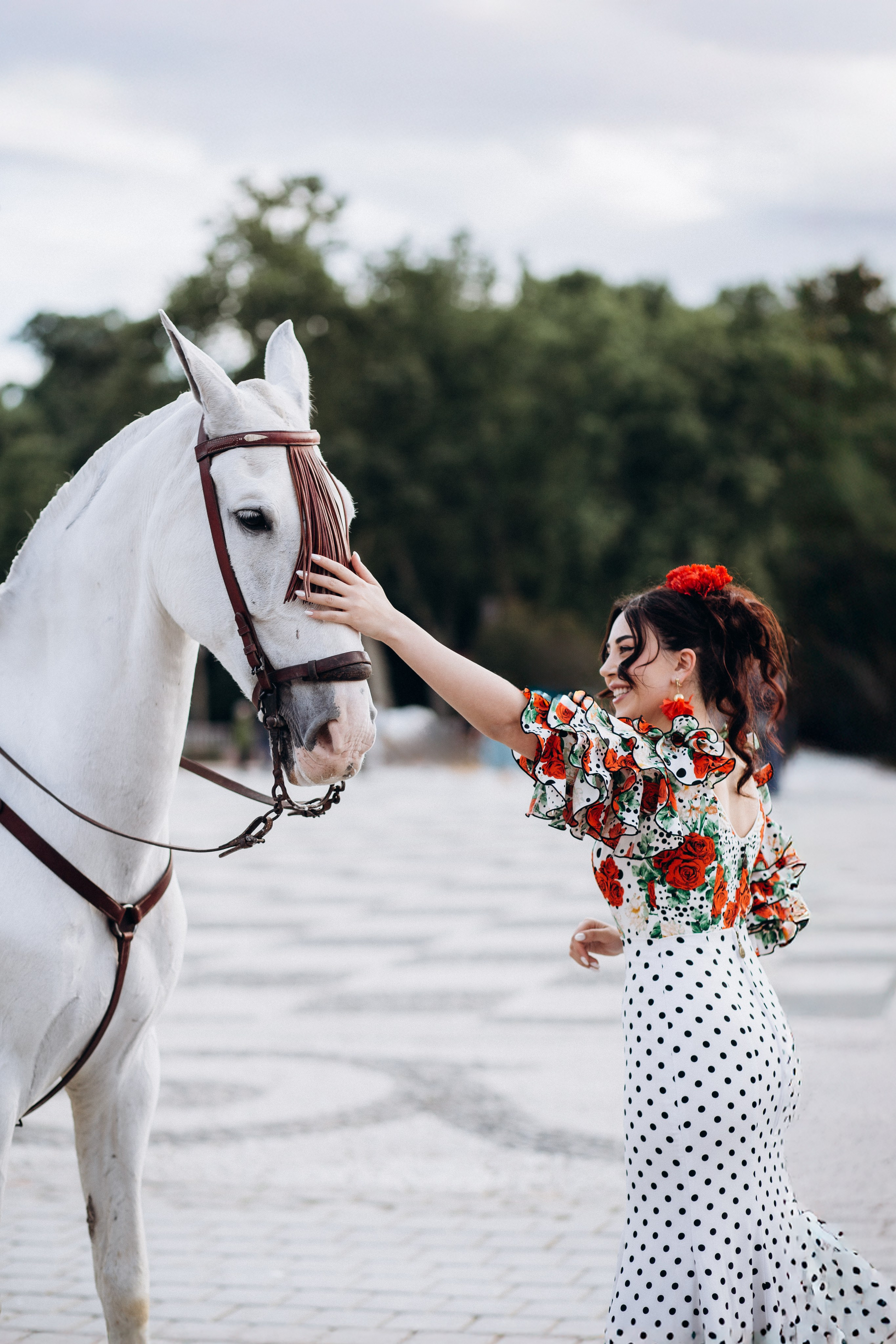Портретная фотосессия в Севилье, Испания — женщина в традиционном платье фламенко нежно прикасается к белой андалузской лошади, воплощая суть испанской элегантности и культурного очарования. Идеально подходит для фотосессий в стиле наследия и с участием животных в Севилье.