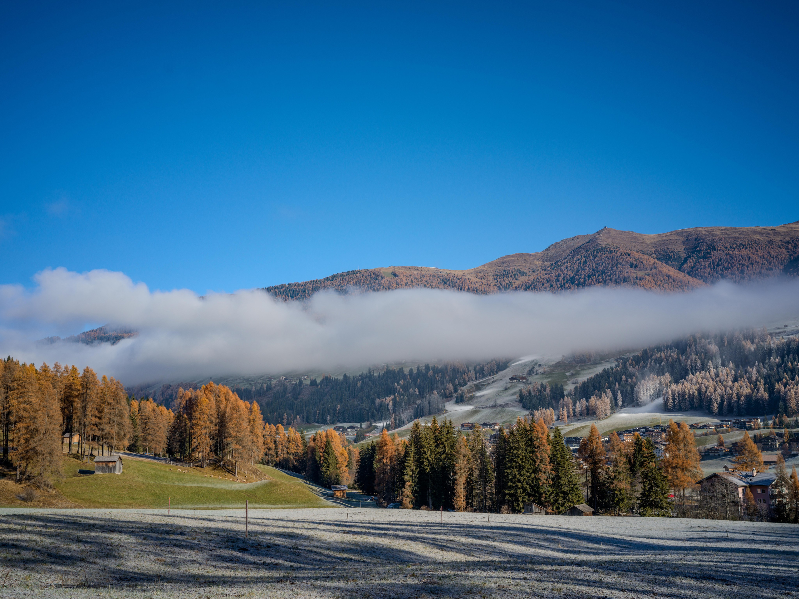 Winter landscape of the Dolomites with low clouds over alpine valley and autumn trees