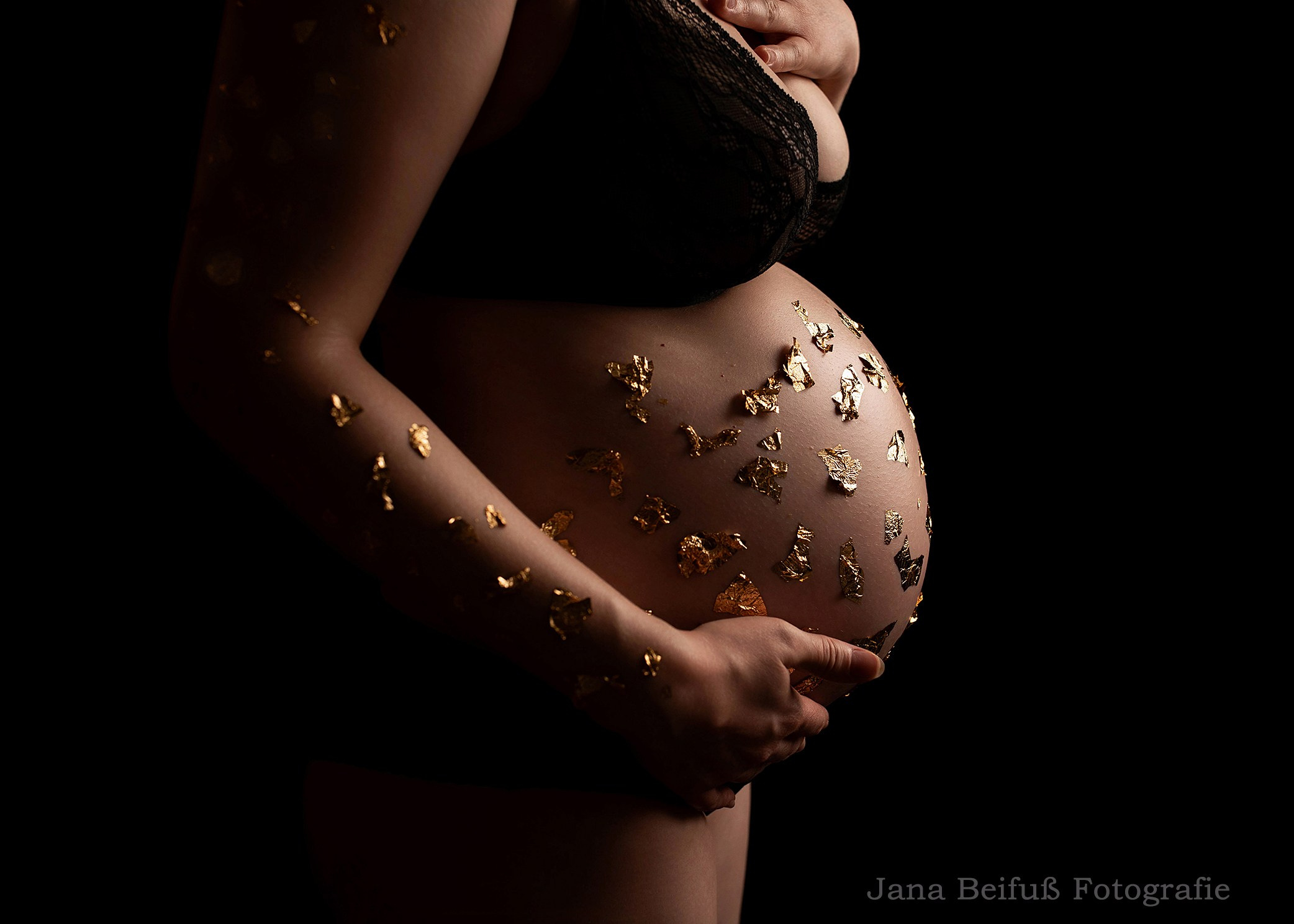 Babybauch in den Händen von werdender Mama in Unterwäsche mit Goldflocken - Schwangerschaftsfotografie Weißenhorn bei Ulm