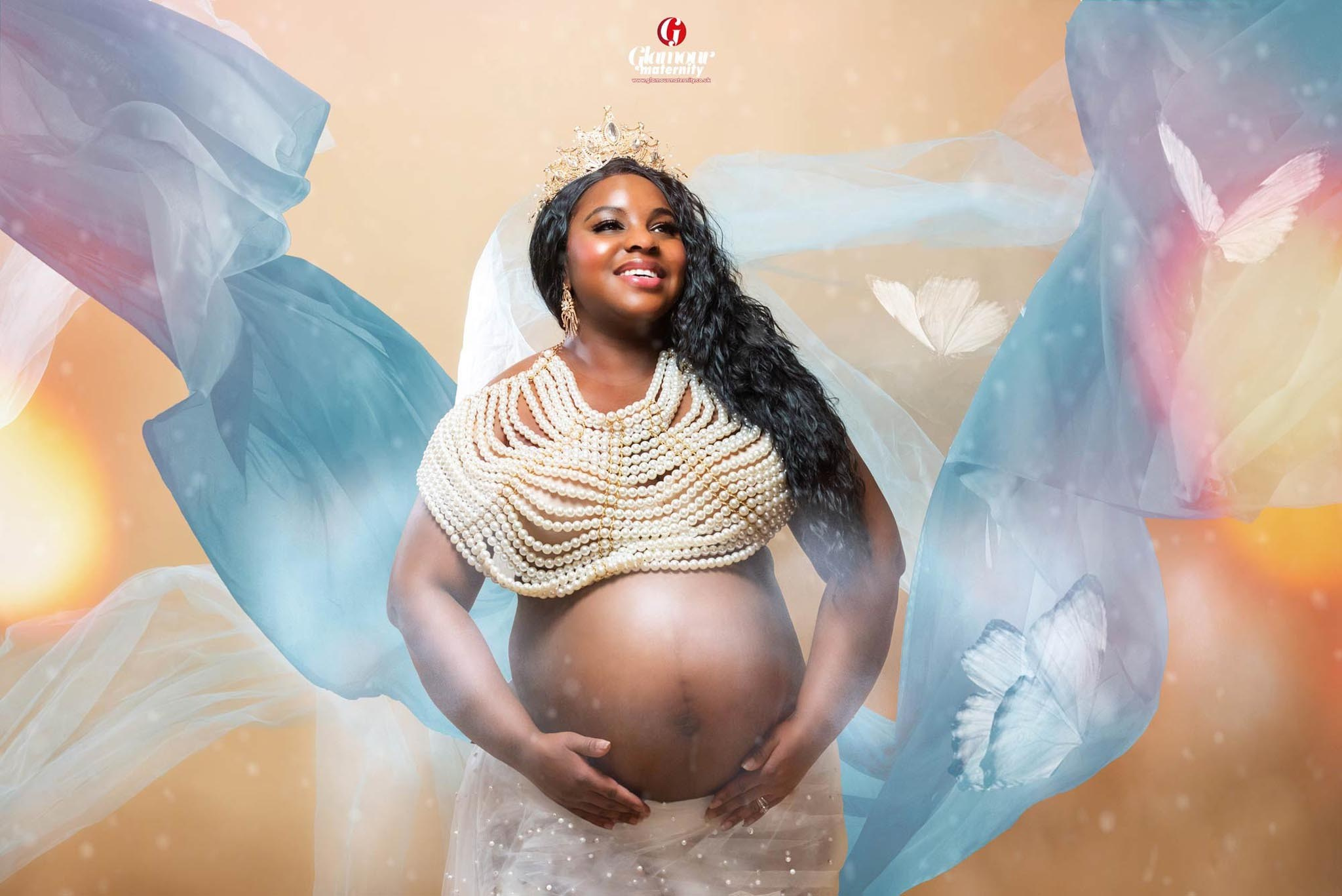 Glamour maternity portrait featuring a crown, pearl styling and flowing blue fabric in an elegant studio setting.