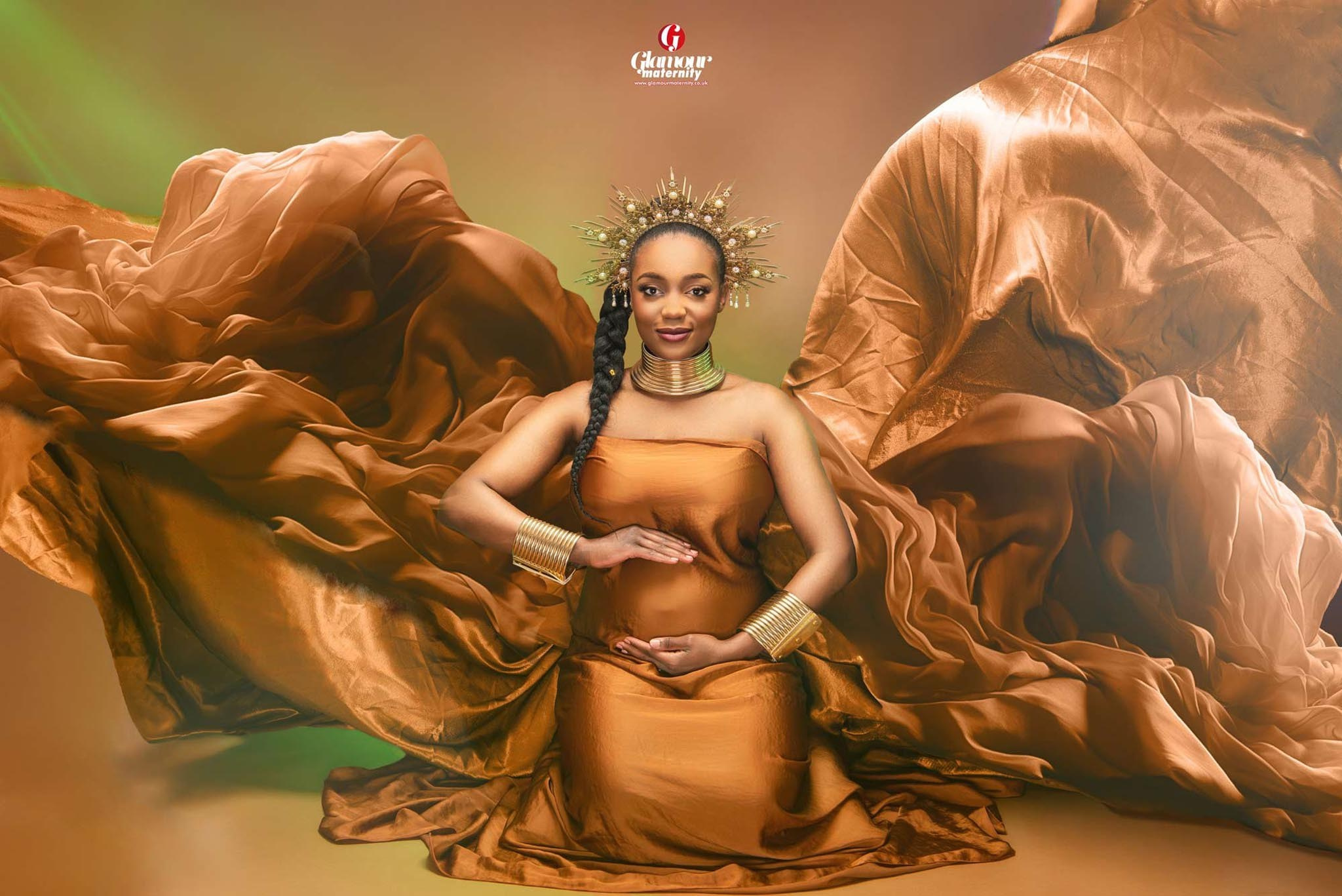 Fashion-inspired maternity portrait in bronze fabric, with an ornate crown, gold jewellery and dramatic flowing material.