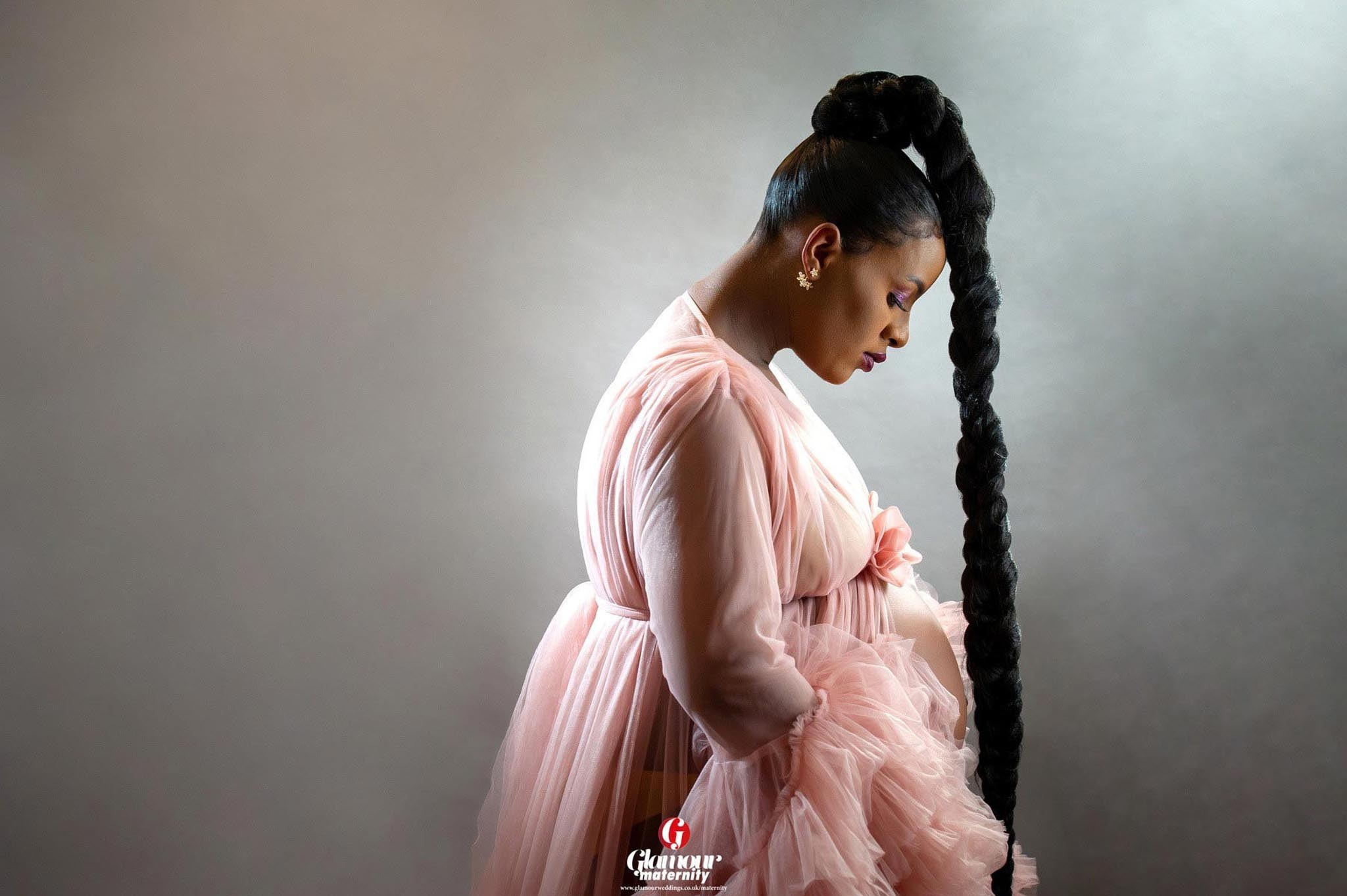 Elegant side-profile maternity portrait in a soft pink gown, highlighting the baby bump with gentle studio lighting.