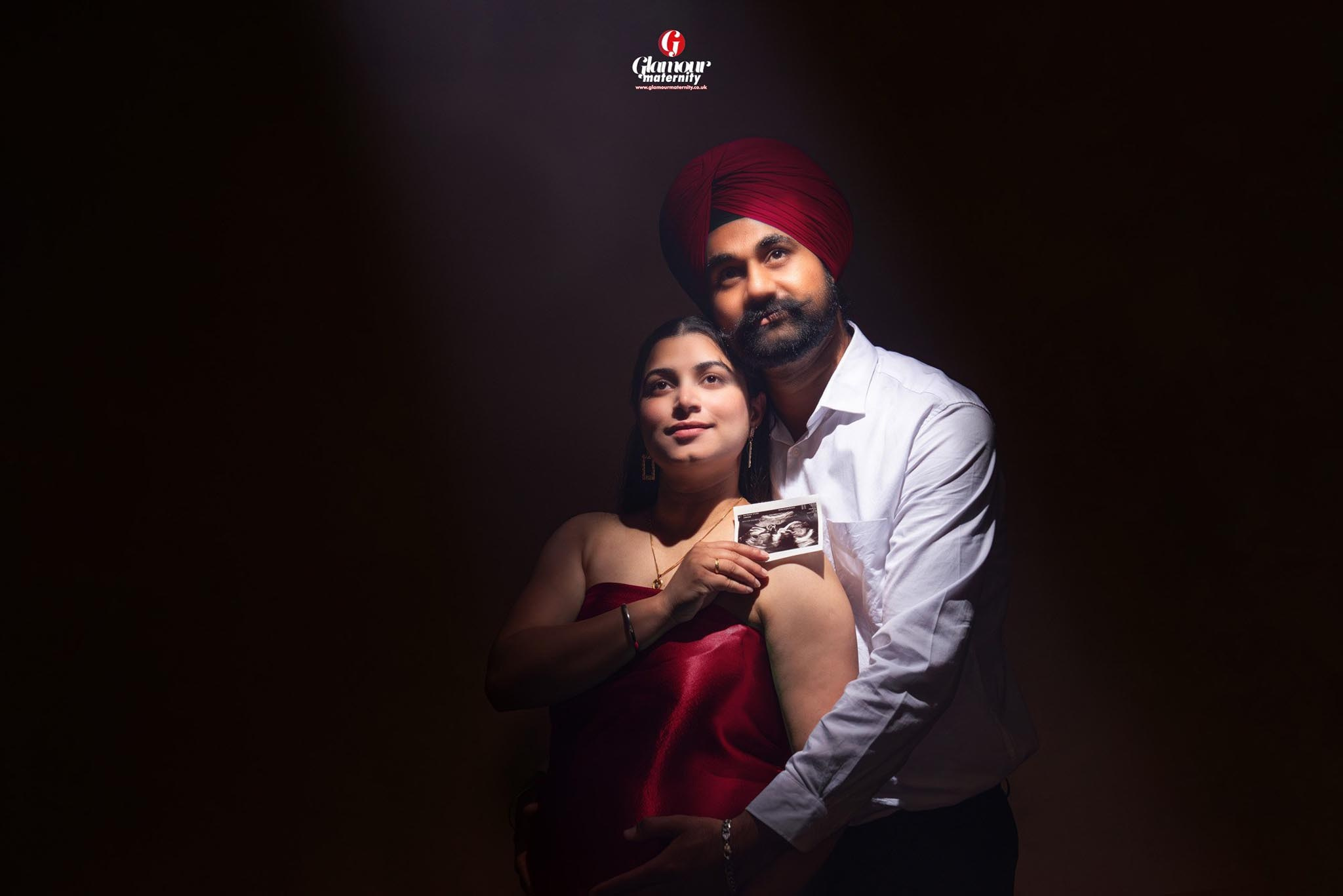 Emotional maternity portrait of an expectant couple holding their baby's ultrasound photo in dramatic, low-key studio lighting.