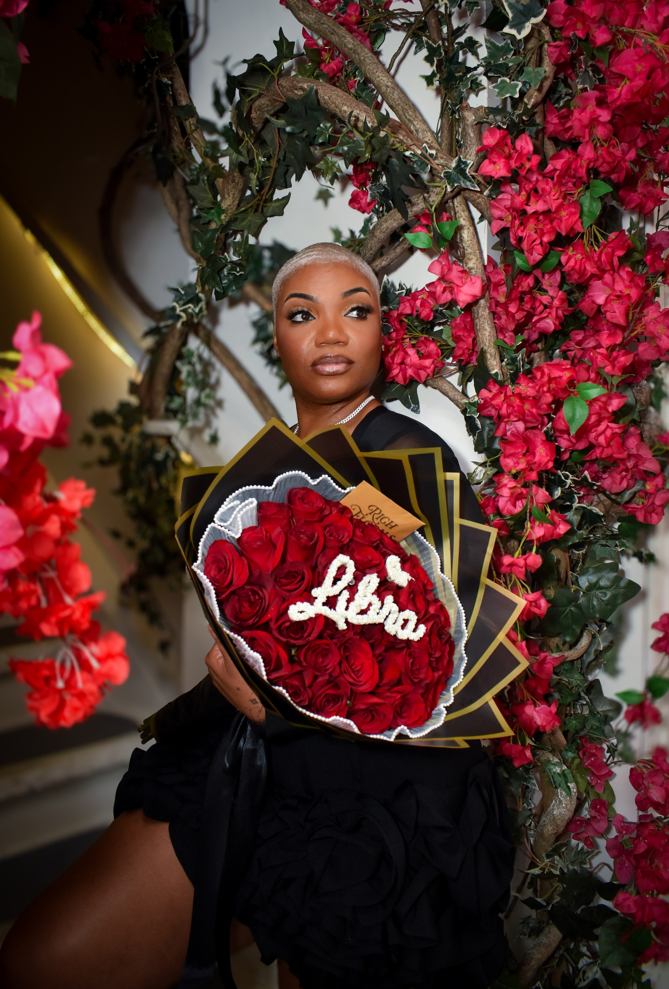 Woman posing with a bouquet in front of a red flower wall, birthday celebration portrait in NYC.