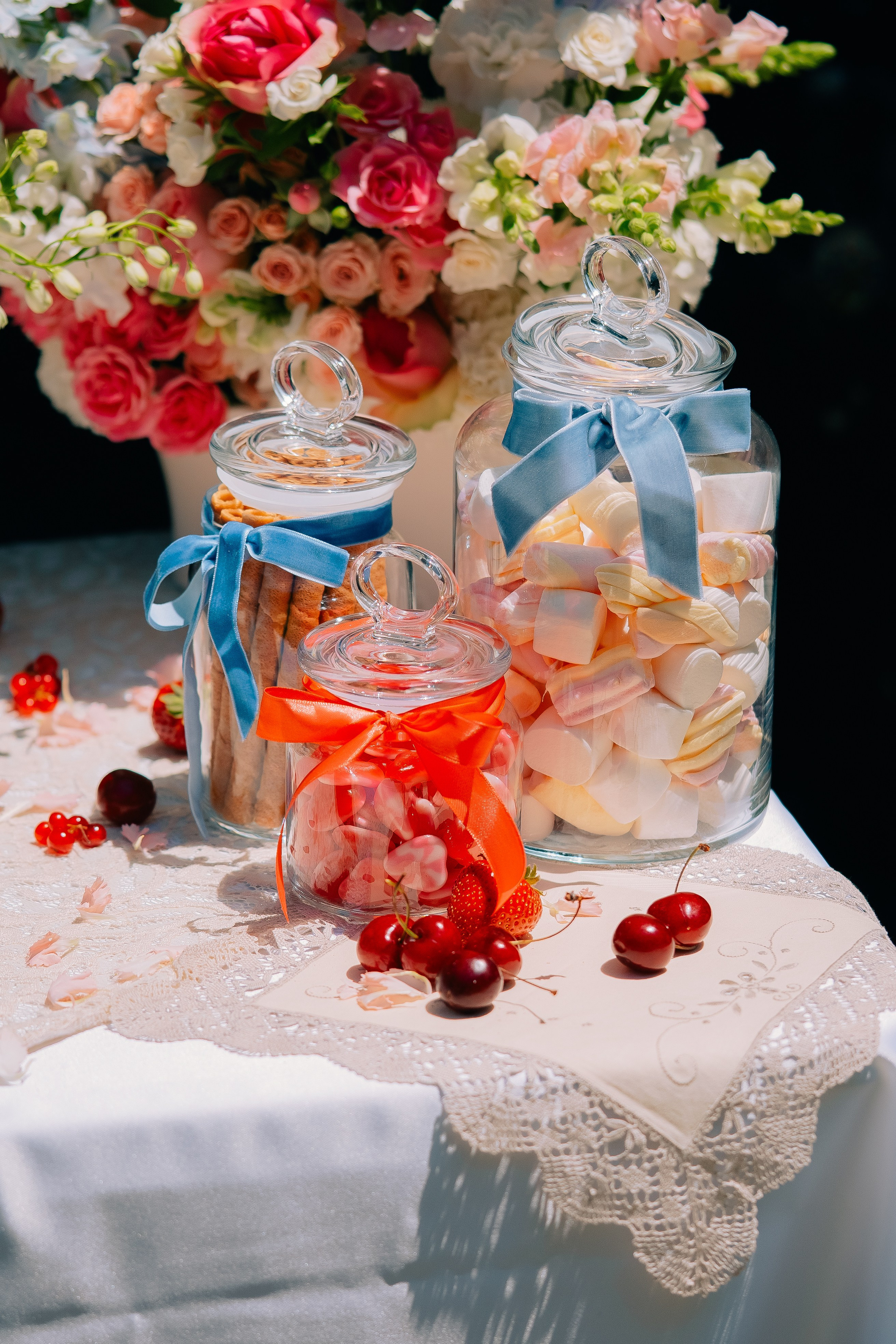 Стеклянные банки со сладостями и ленточками на сладком столе. Элегантные стеклянные банки, наполненные зефиром и конфетами, украшенные синими и красными ленточками, на праздничном сладком столе.