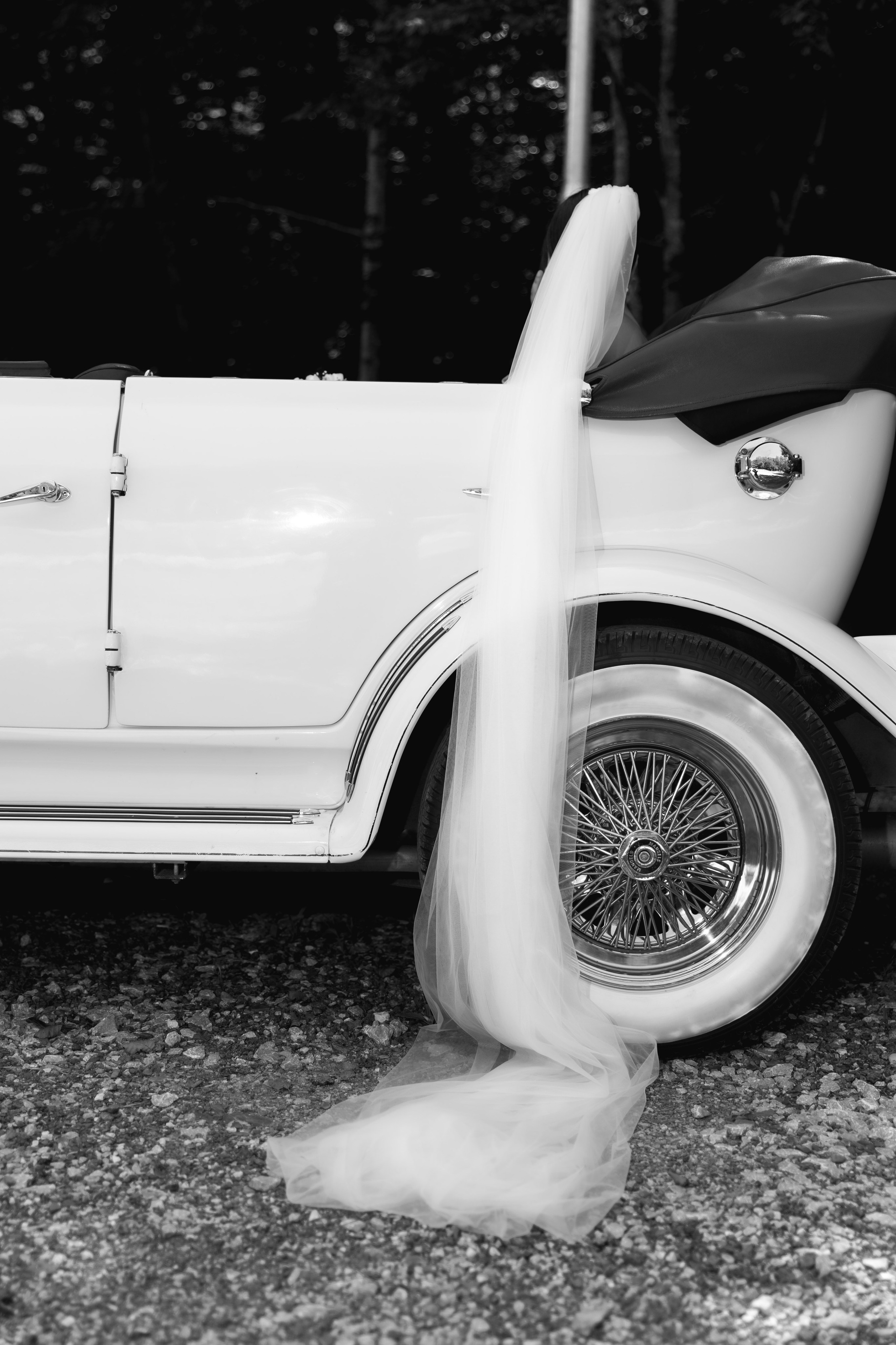 Bride's veil elegantly draped over a classic white vintage car, capturing a timeless wedding detail during the photography session.