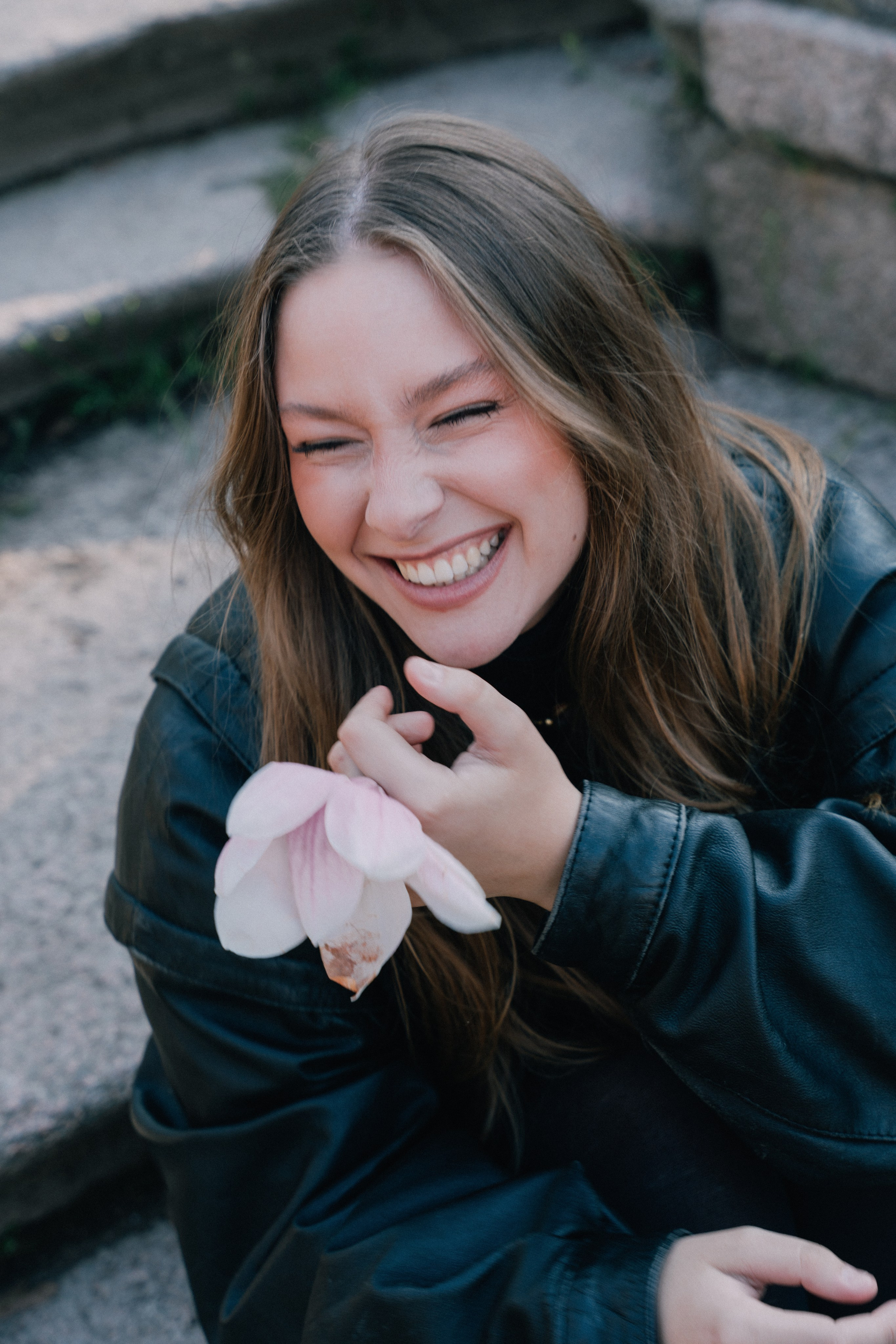 девушка смеется на ступенях в парке в центре Милана в руках у нее цветок магнолии