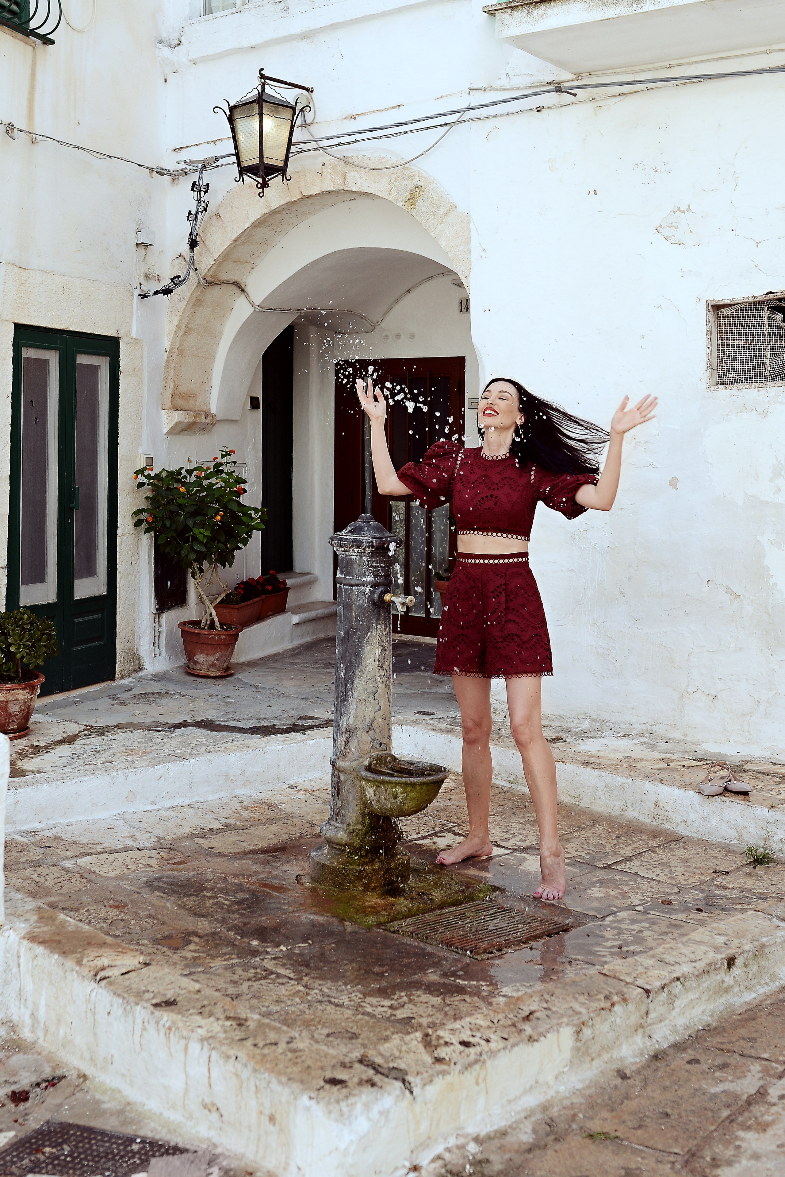 A joyful woman cools off at an old water fountain in a Puglian town Ostuni, playfully splashing water into the air.