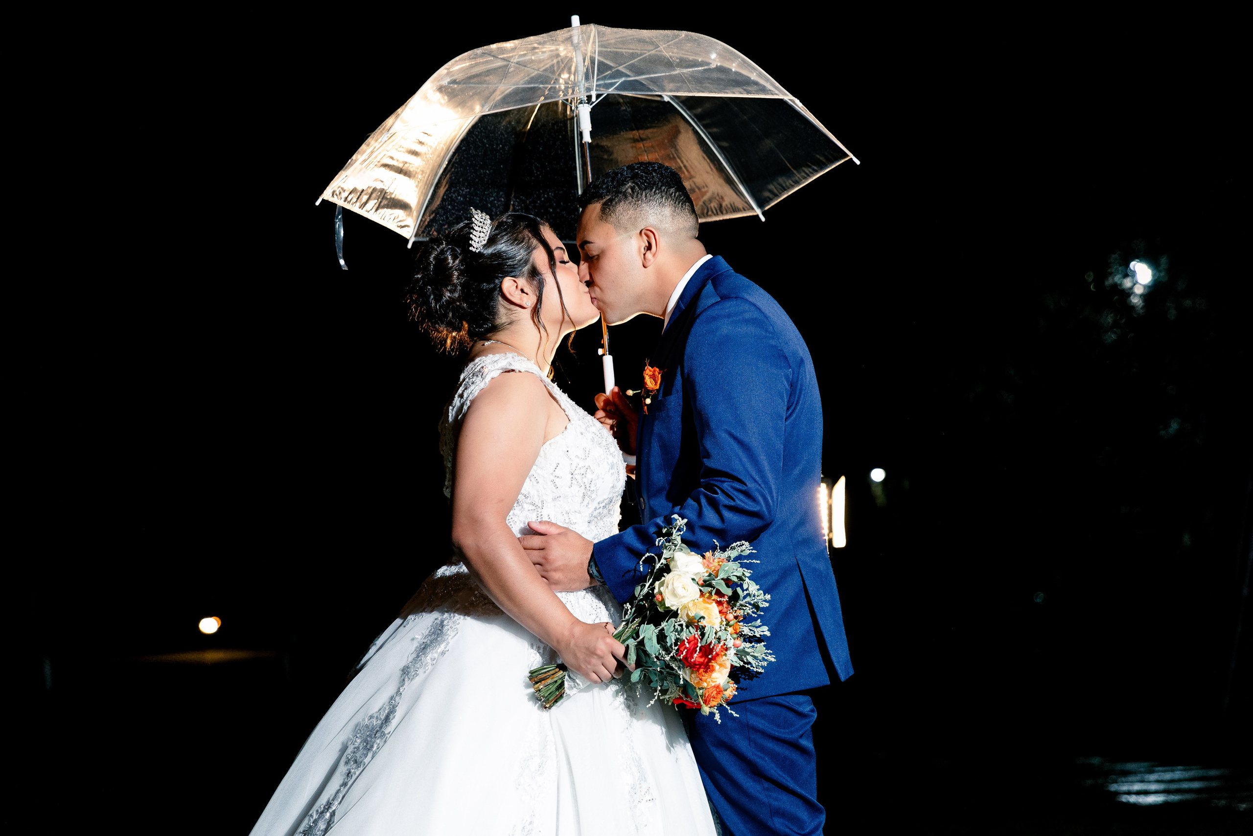 Beijo do casal embaixo do guarda-chuva à noite, com fundo escuro e iluminação dramática.