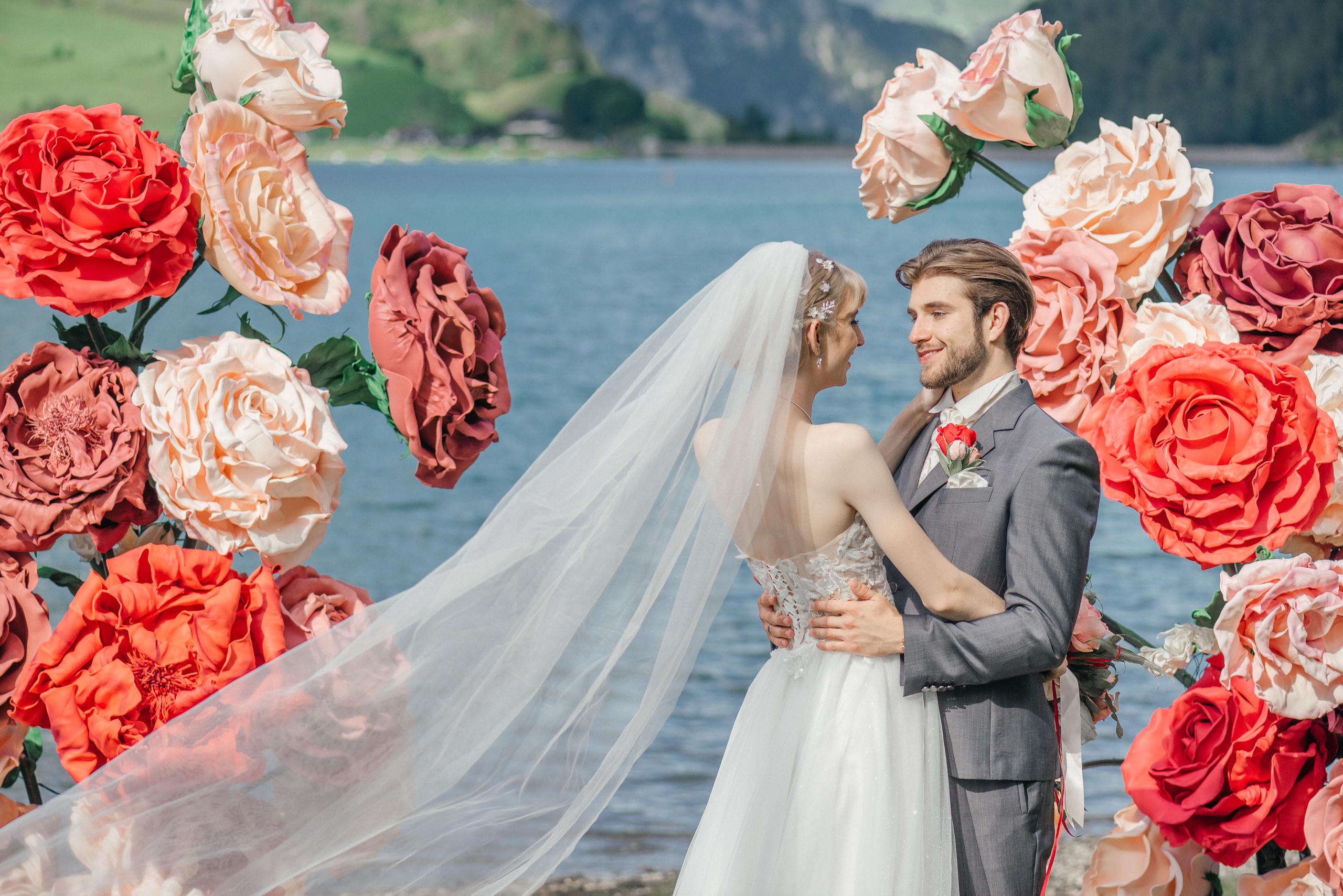 A happy wedding couple on a lake in Switzerland in the swiss mountains with big flowers. Elopement. Bride and fiance. The Alps