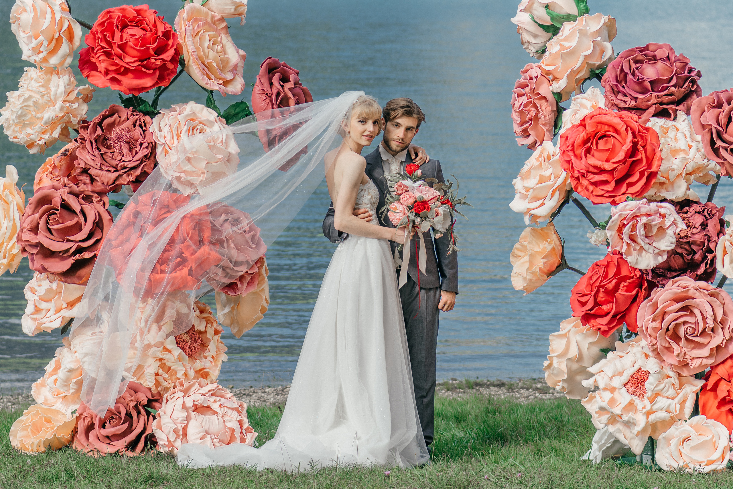 A happy wedding couple on a lake in Switzerland in the swiss mountains with big flowers. Elopement. Bride and fiance. The Alps