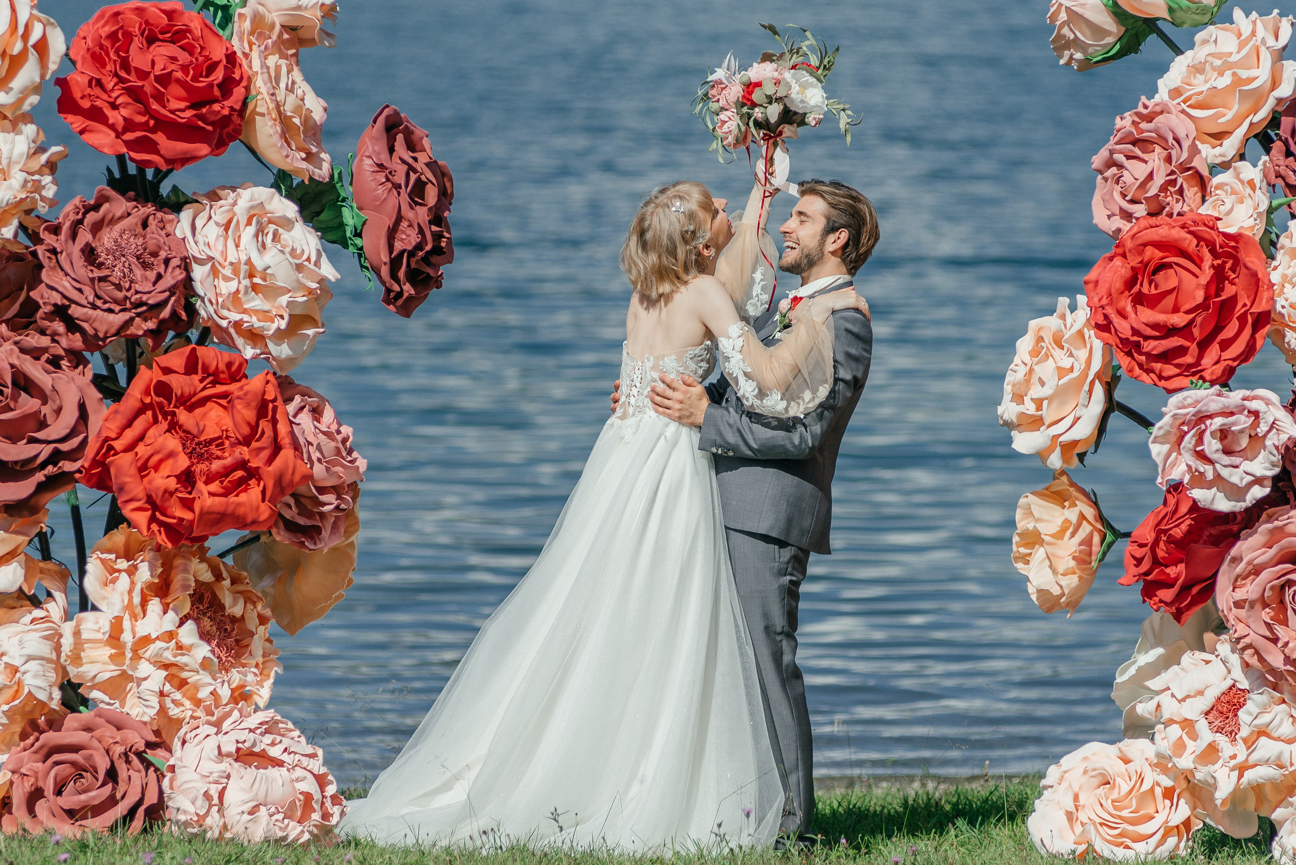 A happy wedding couple on a lake in Switzerland in the swiss mountains with big flowers. Elopement. Bride and fiance. The Alps
