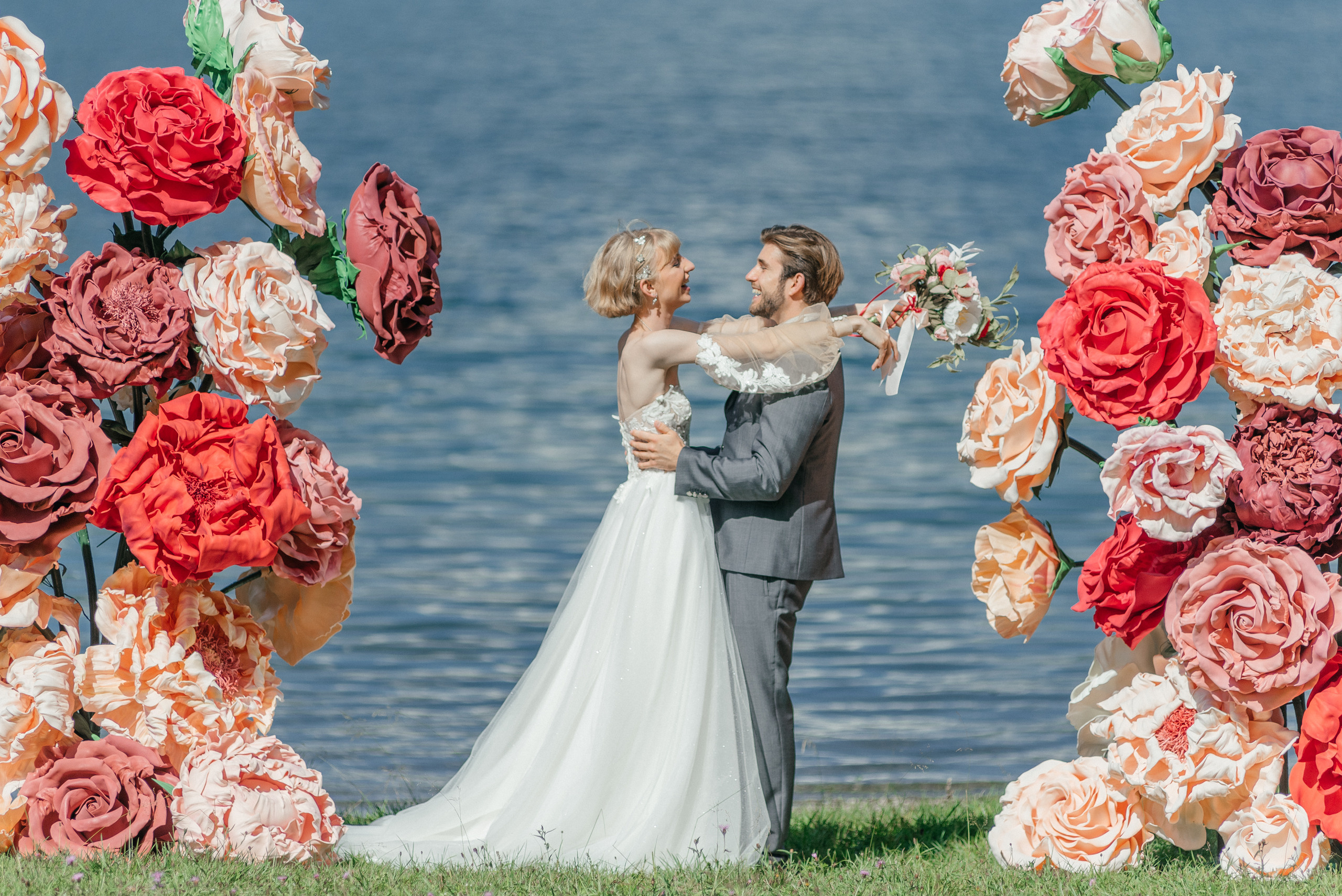 A happy wedding couple on a lake in Switzerland in the swiss mountains with big flowers. Elopement. Bride and fiance. The Alps