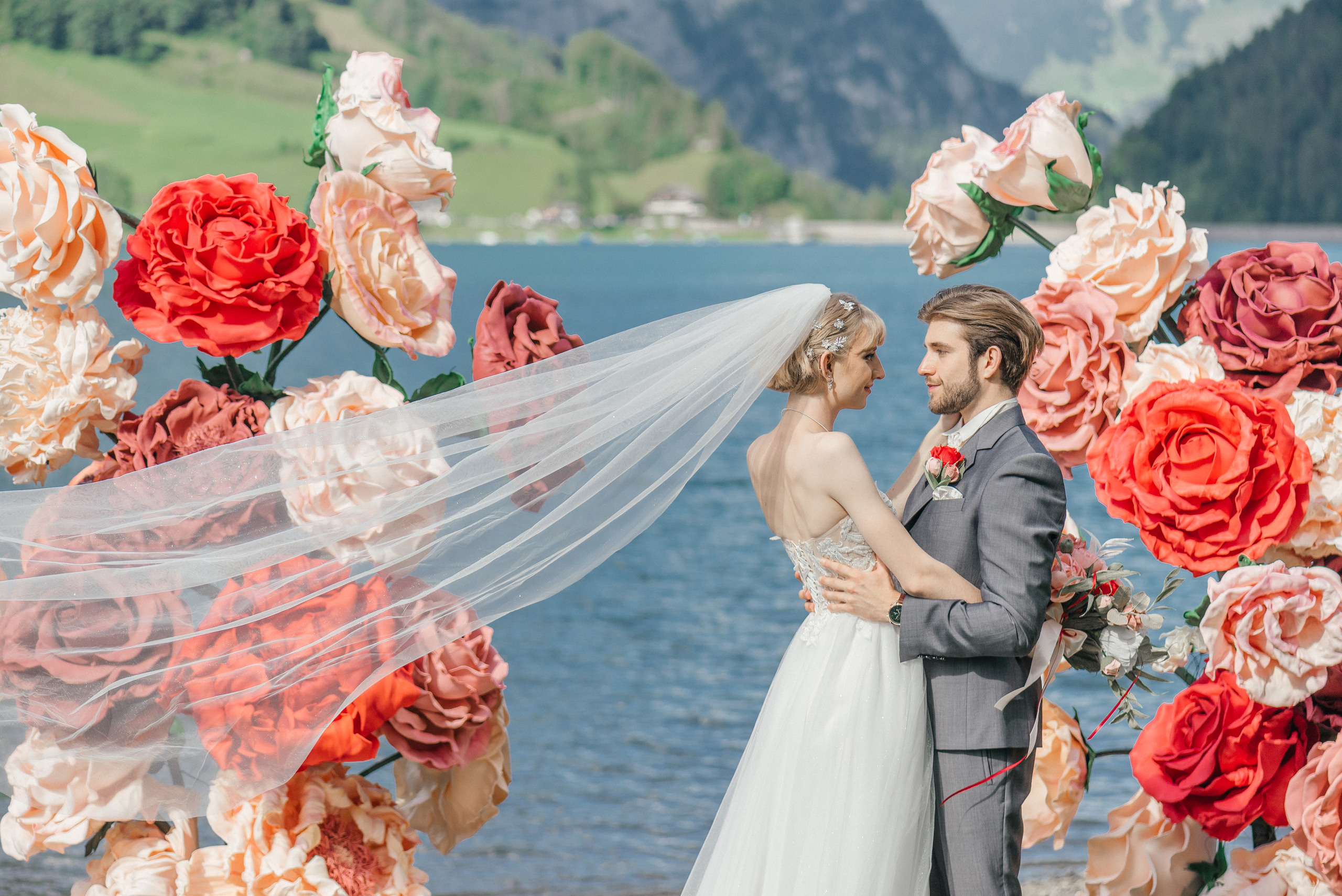 A happy wedding couple on a lake in Switzerland in the swiss mountains with big flowers. Elopement. Bride and fiance. The Alps