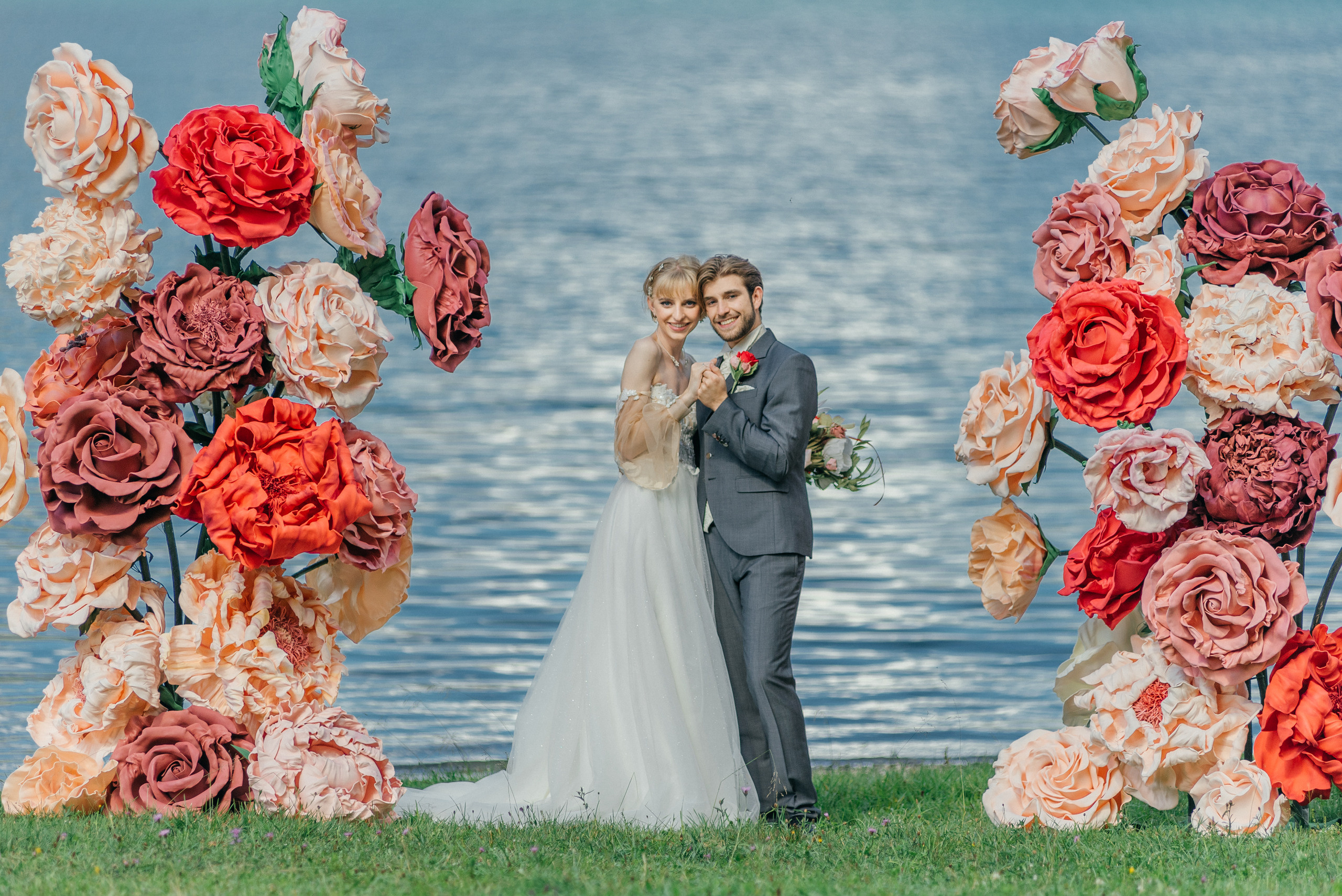 A happy wedding couple on a lake in Switzerland in the swiss mountains with big flowers. Elopement. Bride and fiance. The Alps