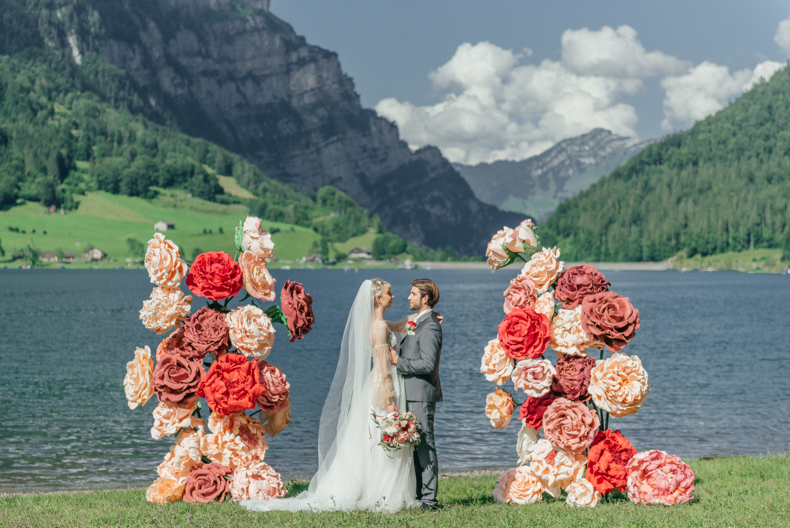 A happy wedding couple on a lake in Switzerland in the swiss mountains with big flowers. Elopement. Bride and fiance. The Alps
