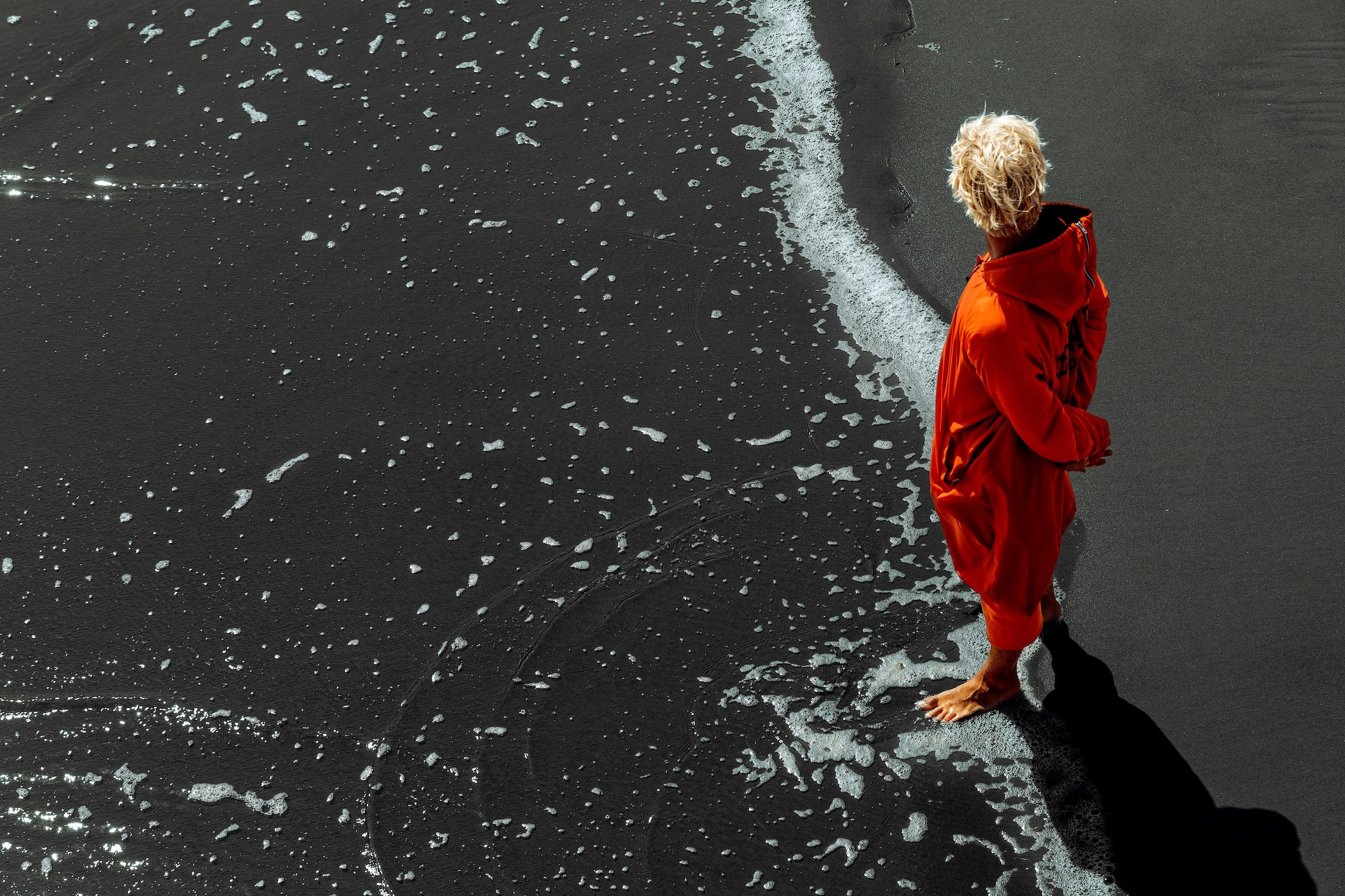 “The last lifeguard”, is a photographic series exploring a solitary figure walking the coastline during low tide. The beach is nearly empty, the water has withdrawn, and the lifeguard — dressed in a red coat — becomes a small yet powerful symbol of human presence within a vast natural space.I am drawn to the tension between responsibility and isolation. A lifeguard is someone whose purpose is to protect others, even when there is no one left on the shore. Walking along an empty beach, the figure becomes a quiet witness, a guardian without an audience.By photographing from above and from a distance, I reduce the human form to a moving mark between sand and sea. The coastline becomes a stage for silence, memory, and observation. These images are not tied to a specific location; they reflect an emotional state — the moment when the world feels both beautiful and emptied, and one person carries the meaning of being there. Denis Bold / Photographer (New York/USA)