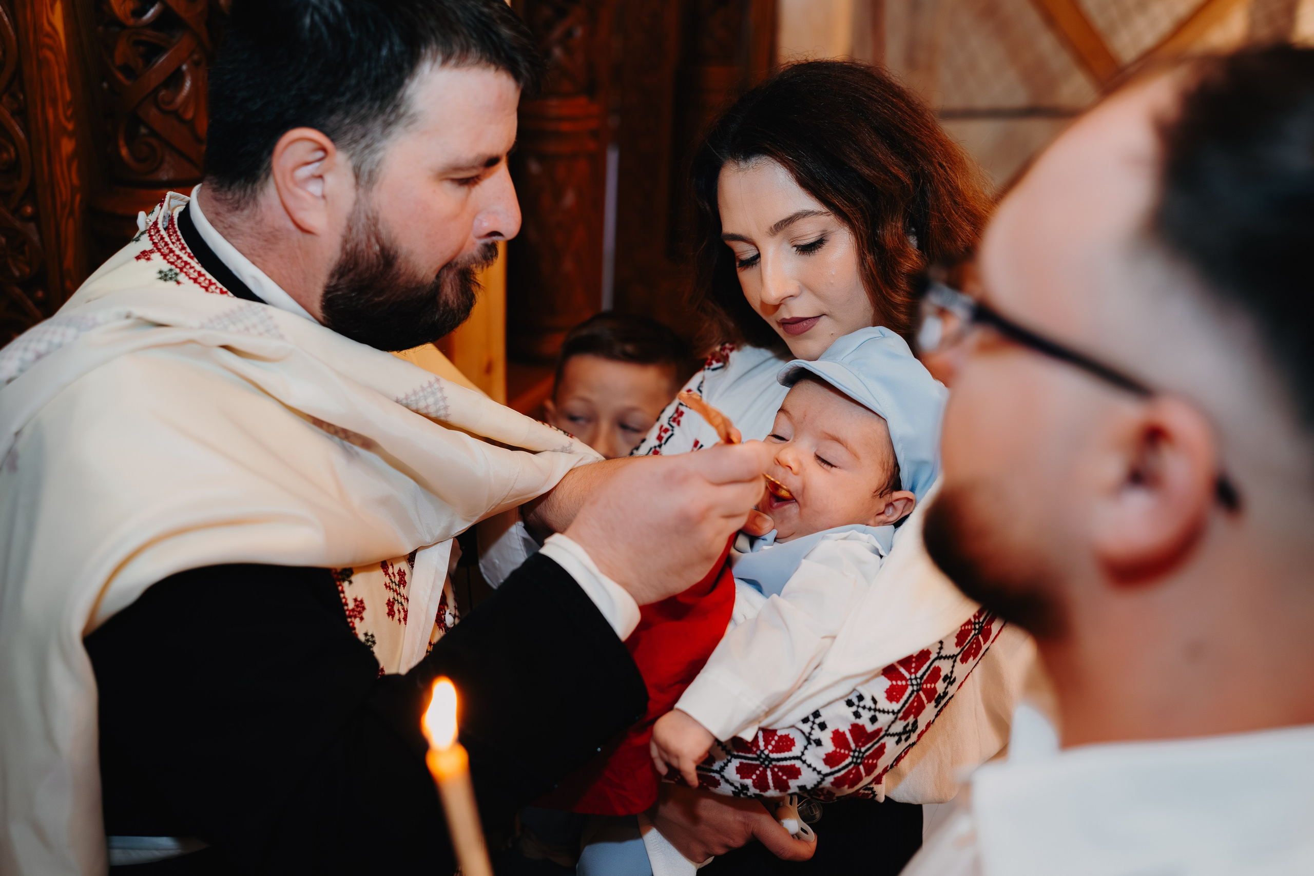 Alt unghi a momentului Împărtășaniei: preotul aduce lingurița cu Sf. Taină către gura pruncului Arthur Mihail, în timp ce nașa îl ține cu grijă. Detaliul concentrat al ritualului final, într-o atmosferă profundă de reculegere în Catedrala Bârlad.