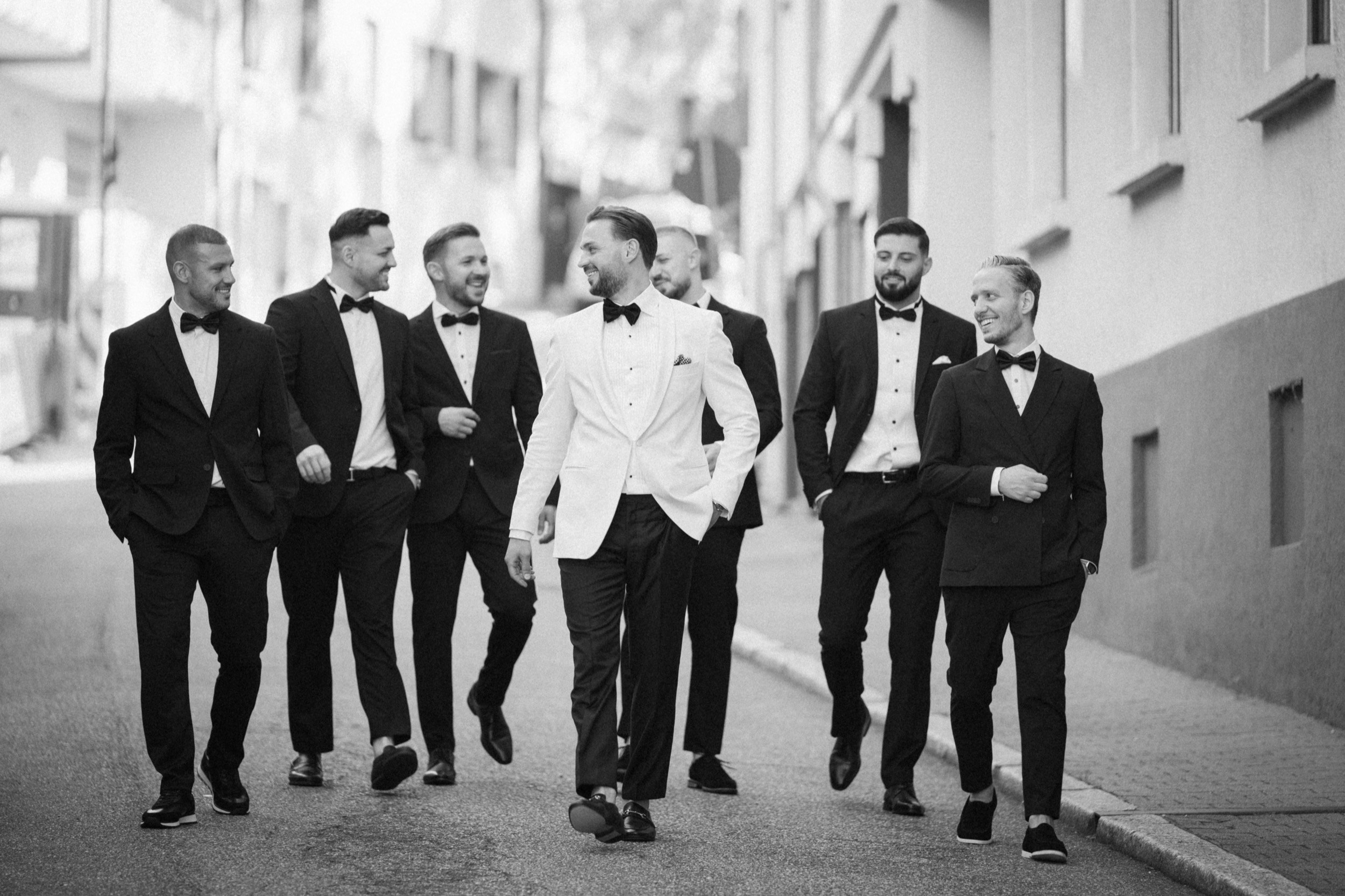 Bräutigam und seine Freunde in Smokings gehen durch eine Straße in Baden-Baden, Schwarzweißfoto