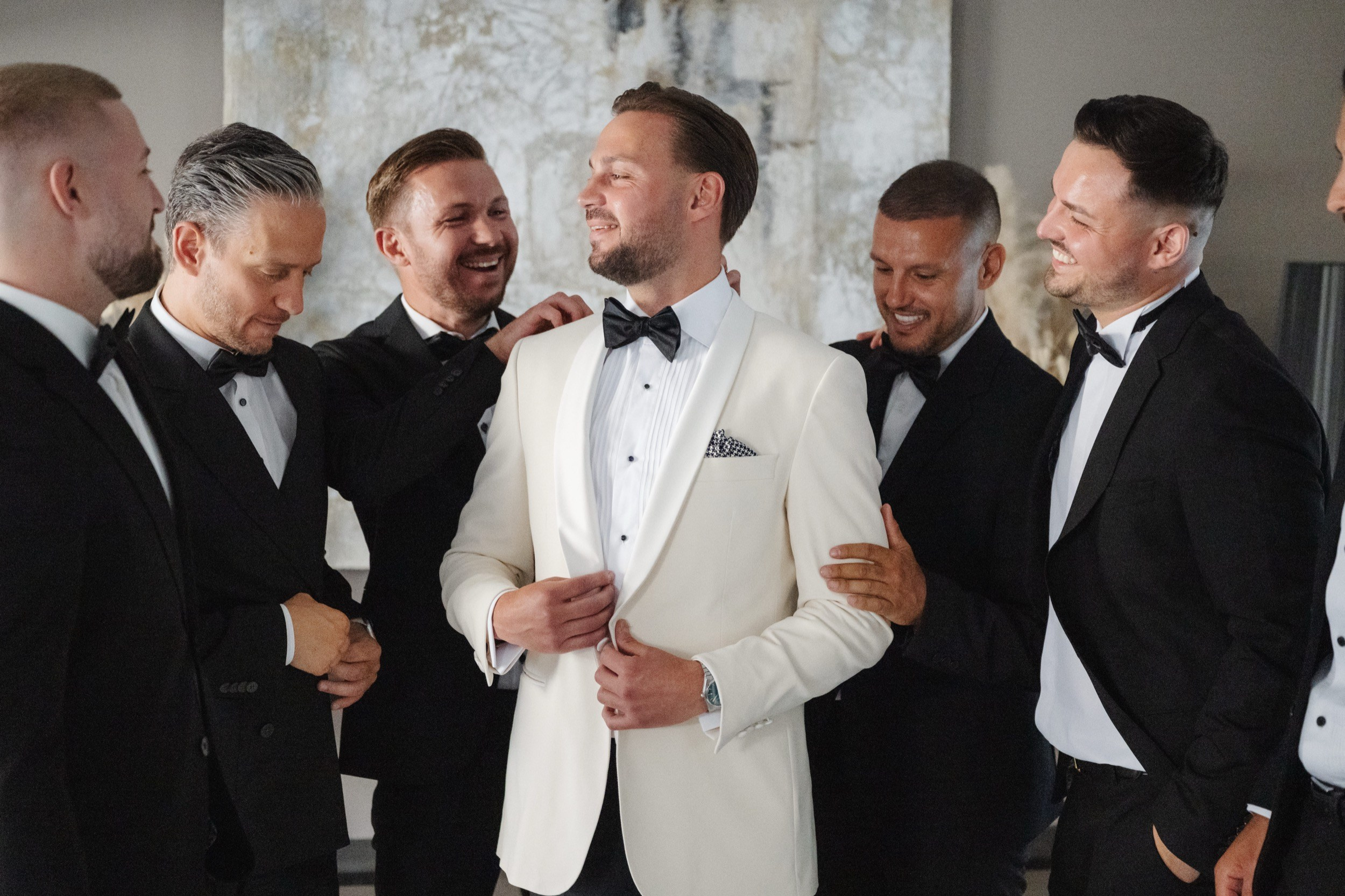 Bräutigam im weißen Dinnerjacket mit seinen Freunden in schwarzen Smokings beim Getting Ready