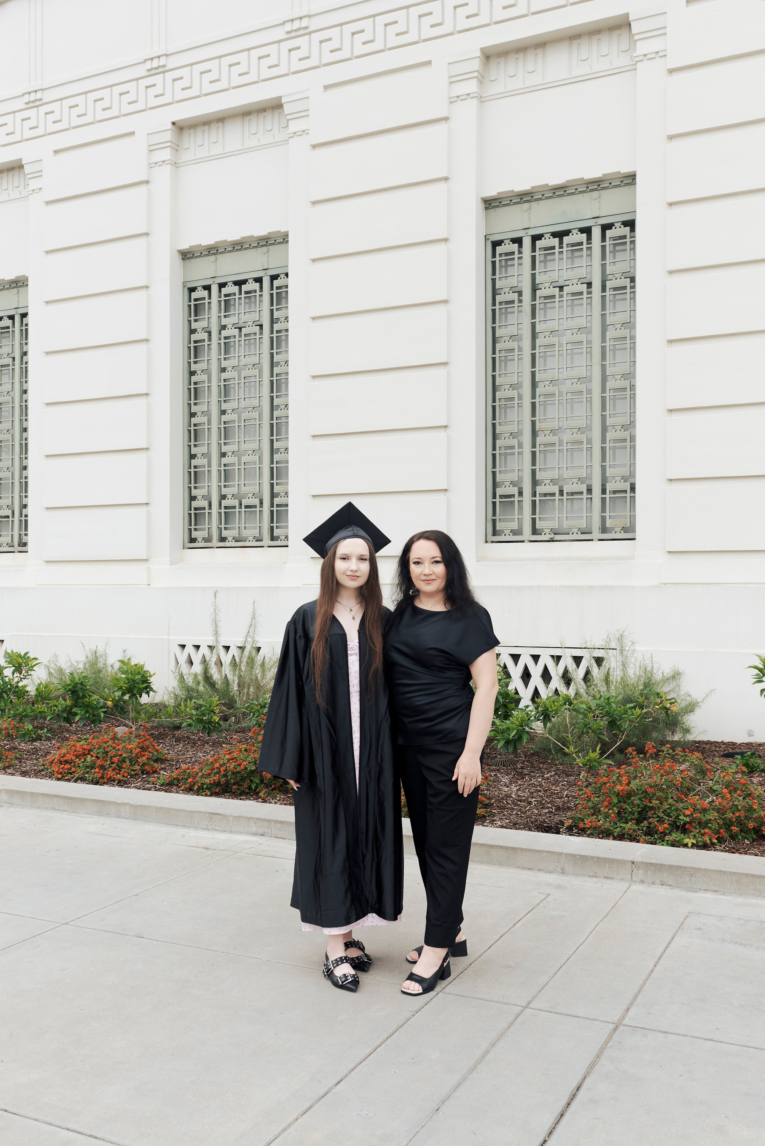 Graduate in formal attire and cap holding a diploma at a scenic Los Angeles overlook