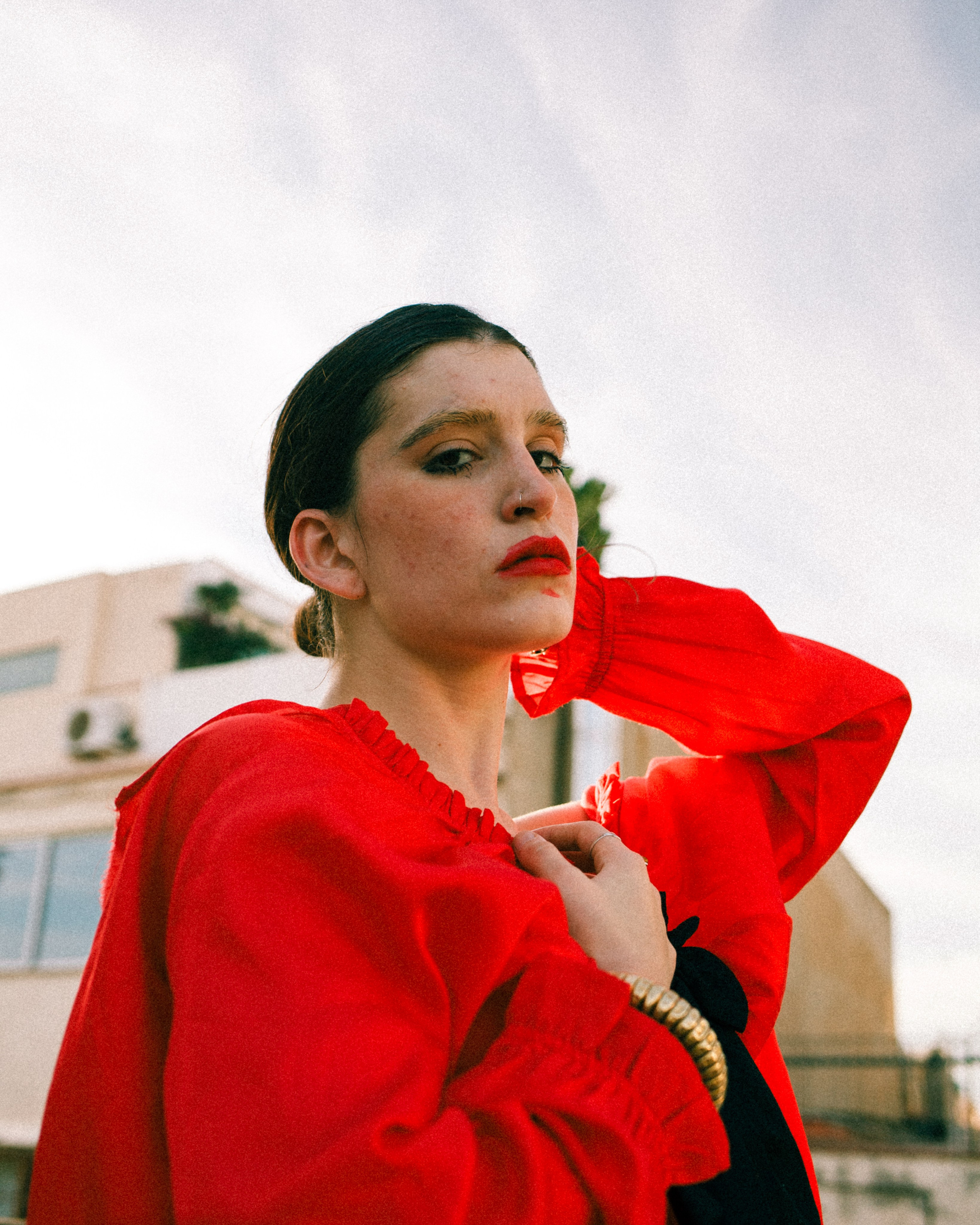 Woman in red outfit gazing to the side against a rooftop sky