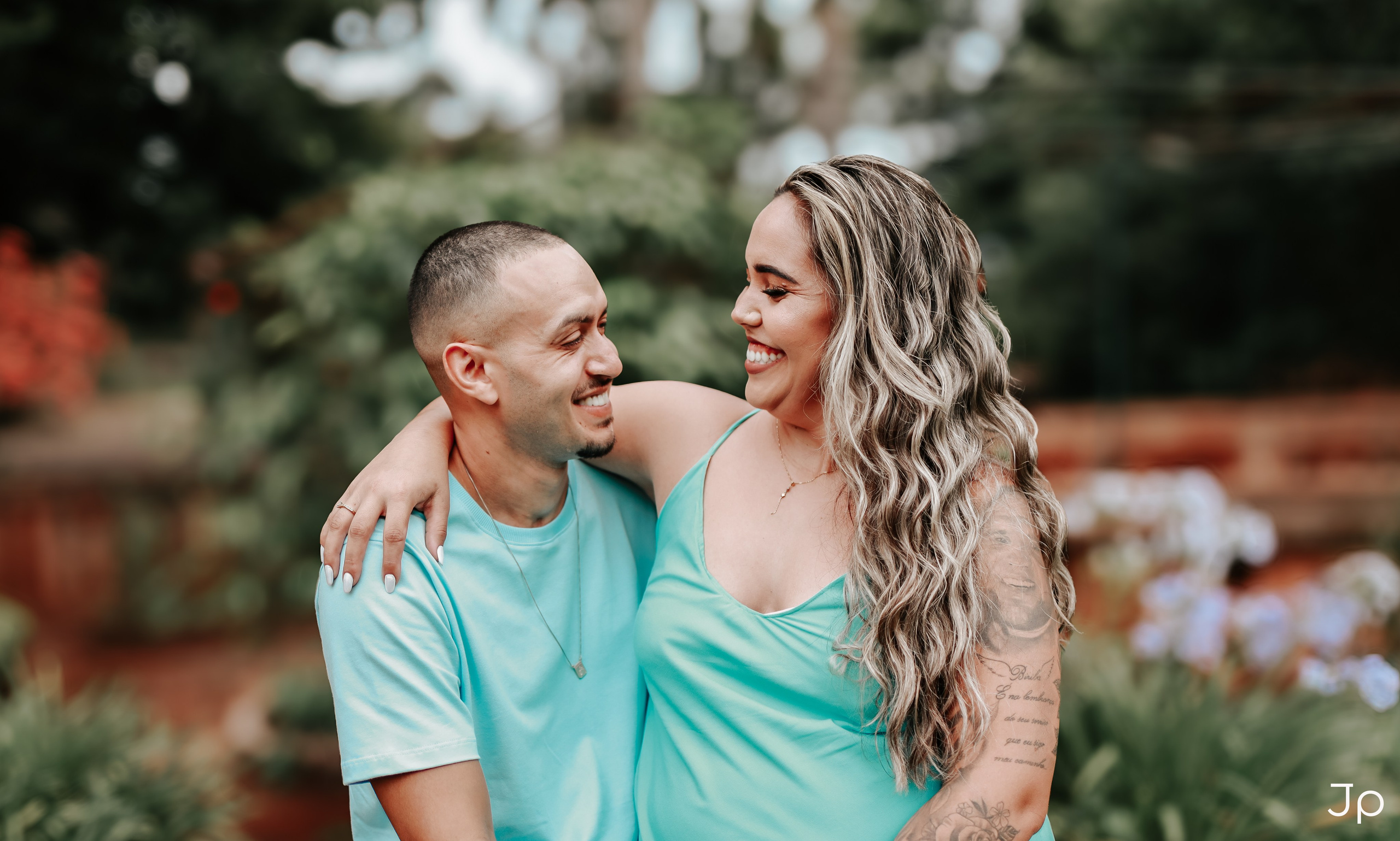 Fotógrafo em Pederneiras registra carinho do casal em jardim florido durante ensaio externo.