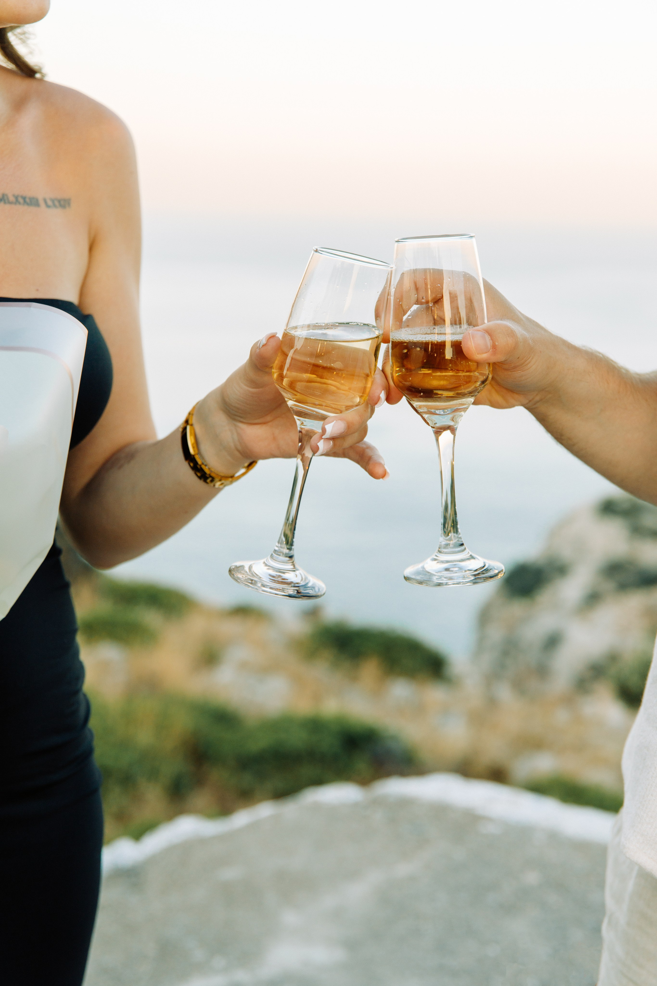 "Anstoßen auf die Liebe: Ein Paar genießt ein Glas Sekt nach dem Heiratsantrag auf dem Profitis Ilias, hoch über der Küste von Faliraki und dem azurblauen Mittelmeer."