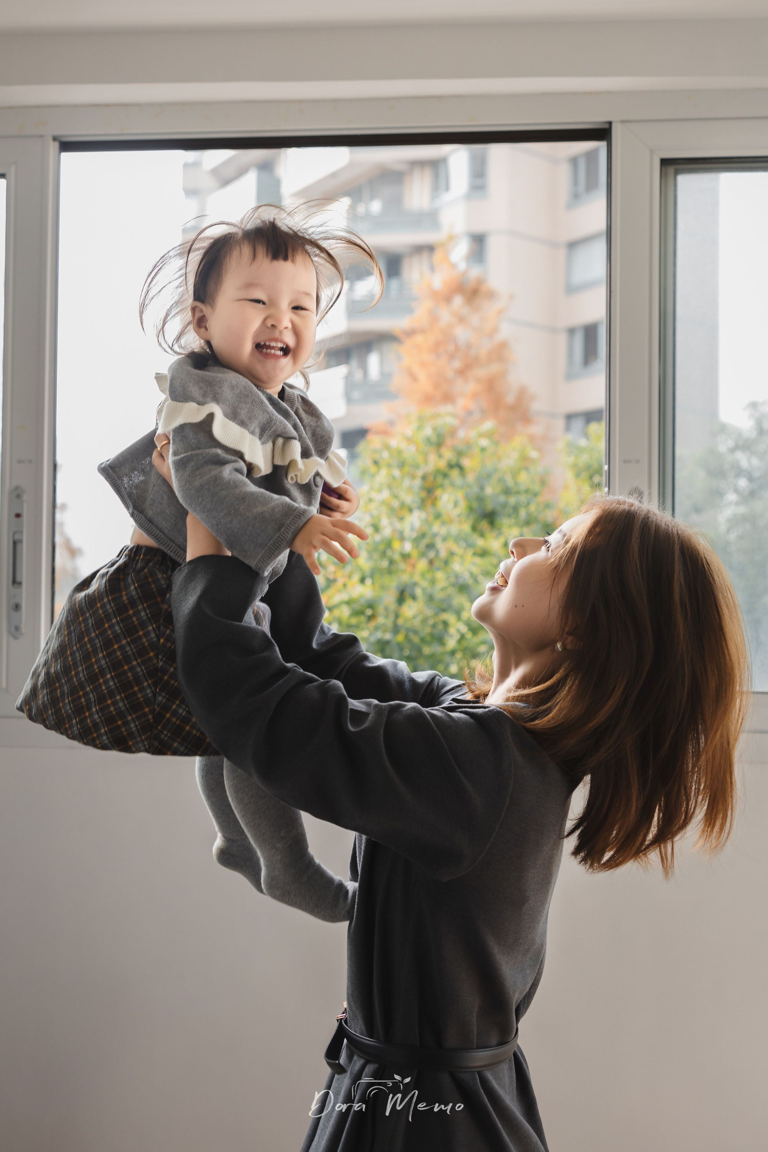 Mom lifting her toddler up in the air near a window, joyful family interaction during a documentary photo session in Shanghai.