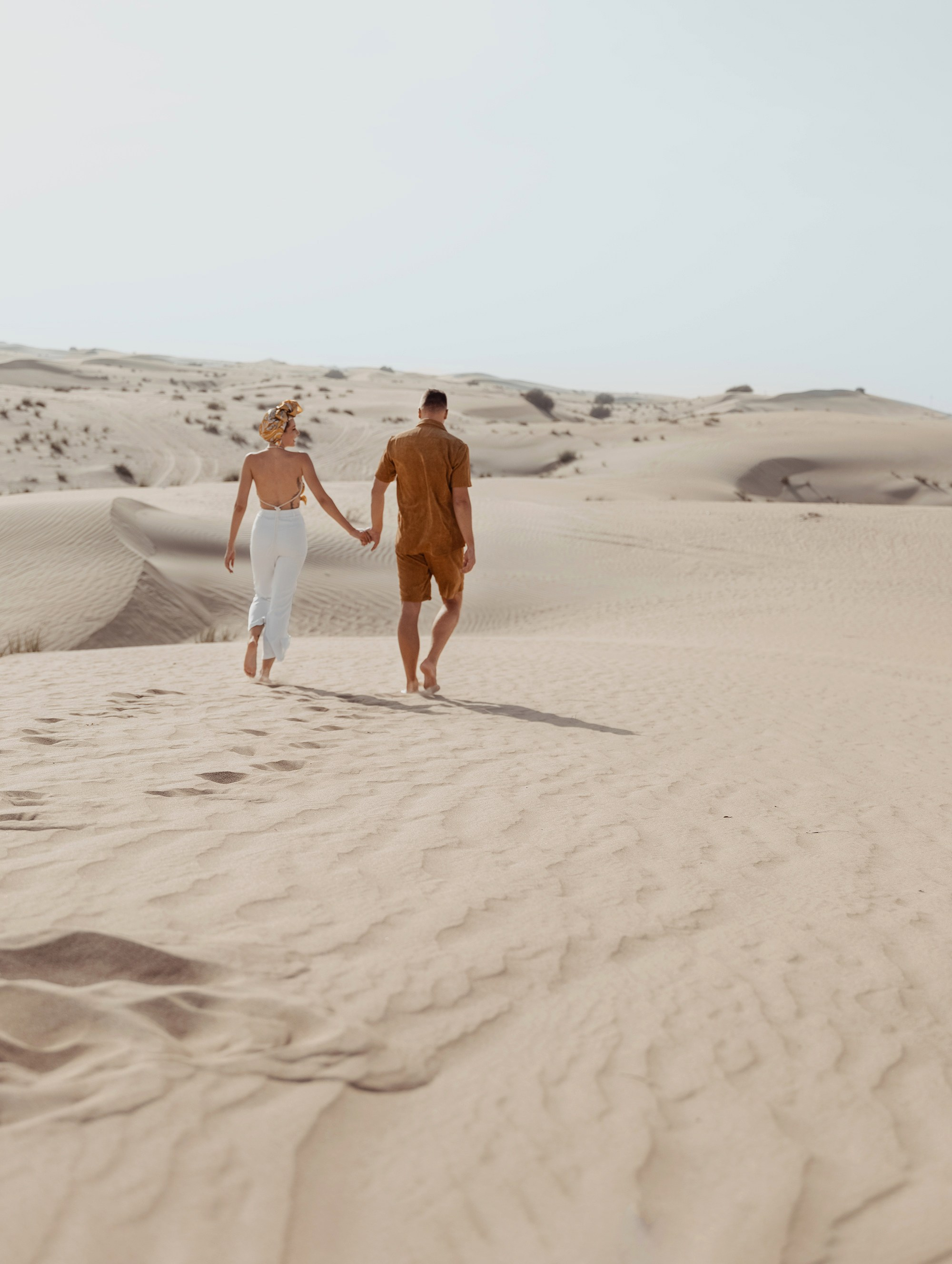 two lovers share a joyful embrace in the middle of a vast desert, surrounded by endless sand and a clear blue sky. Dubai, United Arab Emirates