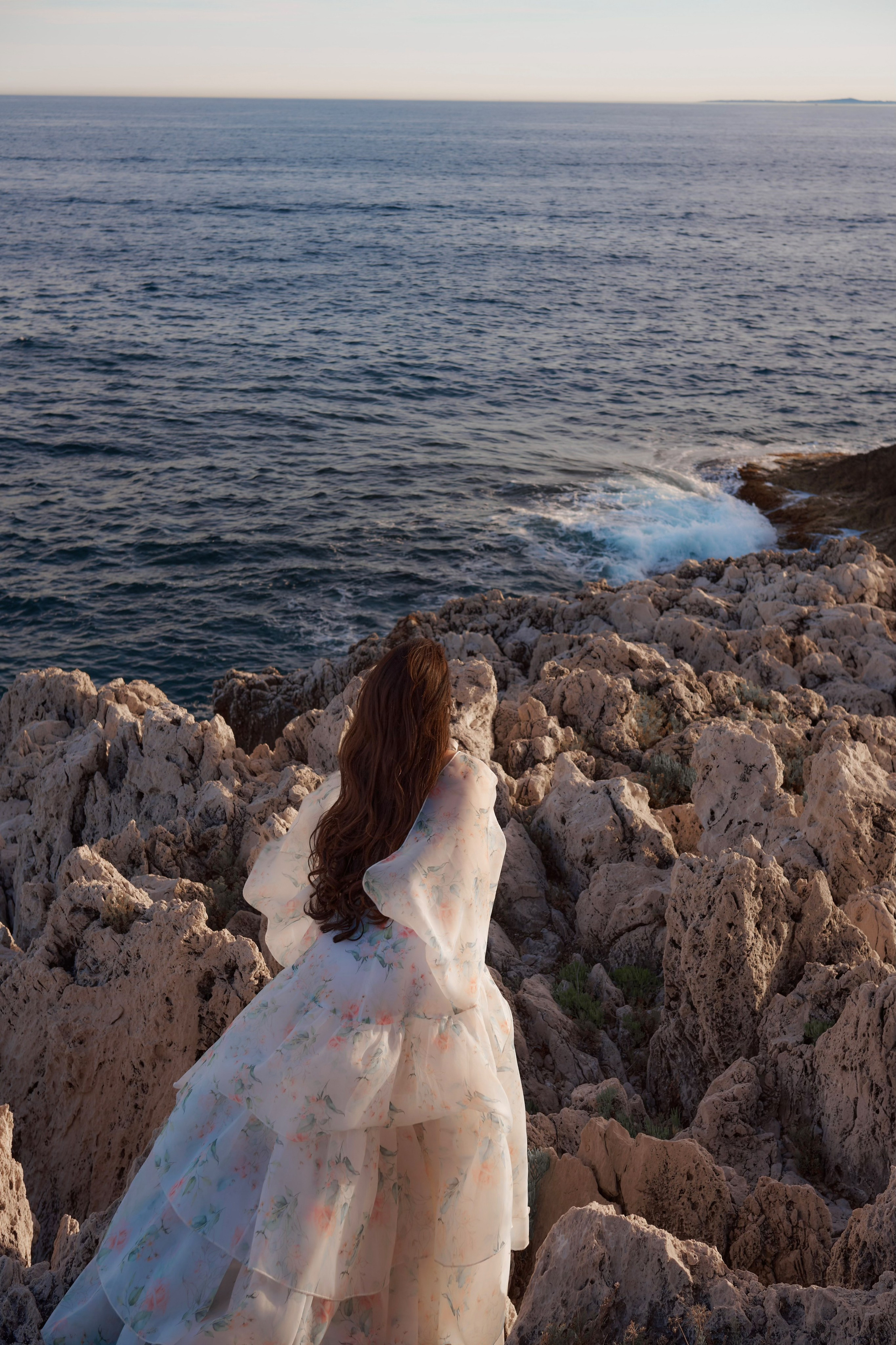 Elegant woman in flowing organza dress standing on cliffs with sea view Saint-Jean-Cap-Ferrat