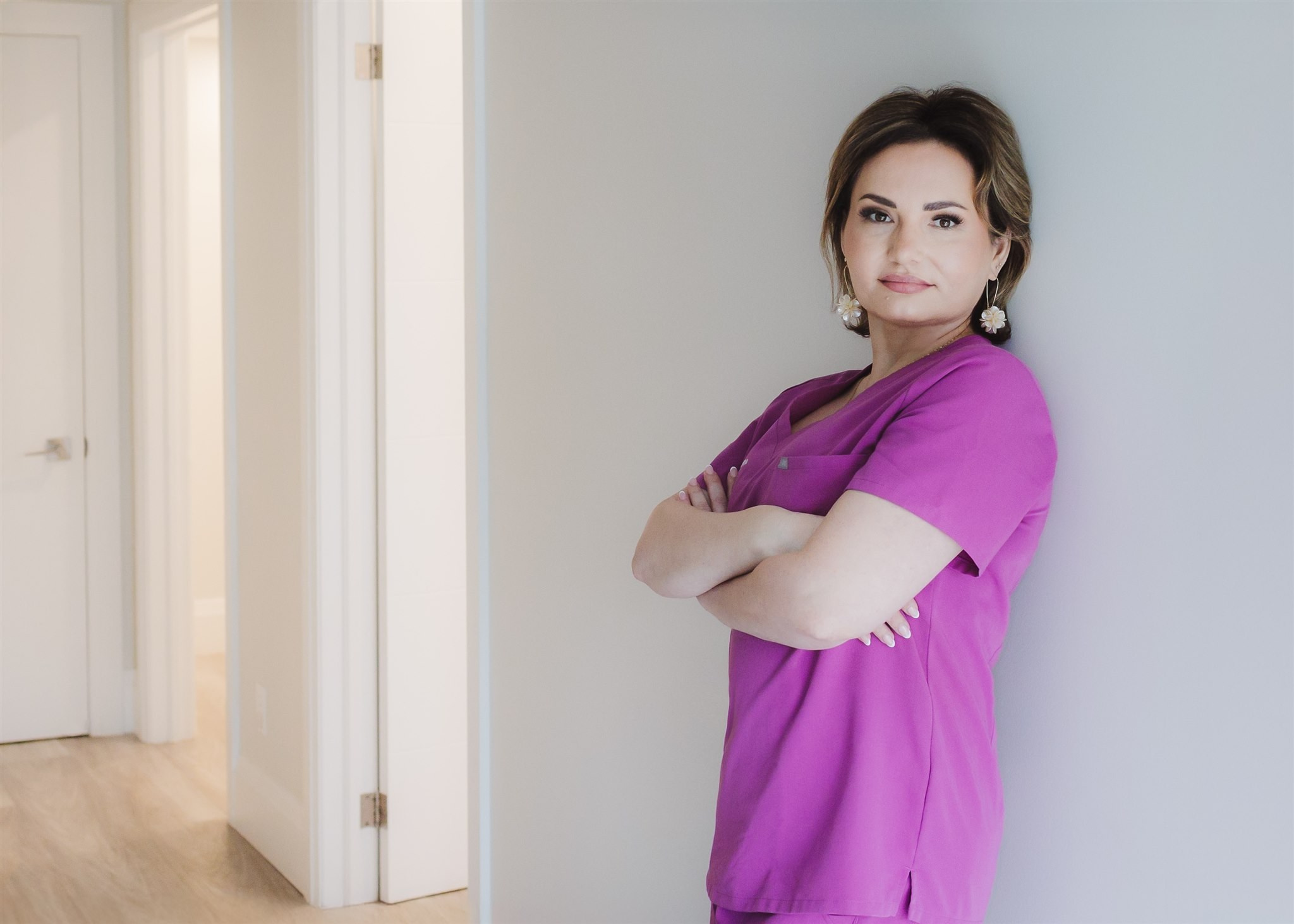 branding portrait of a woman in pink scrubs leaning against the wall in her salon