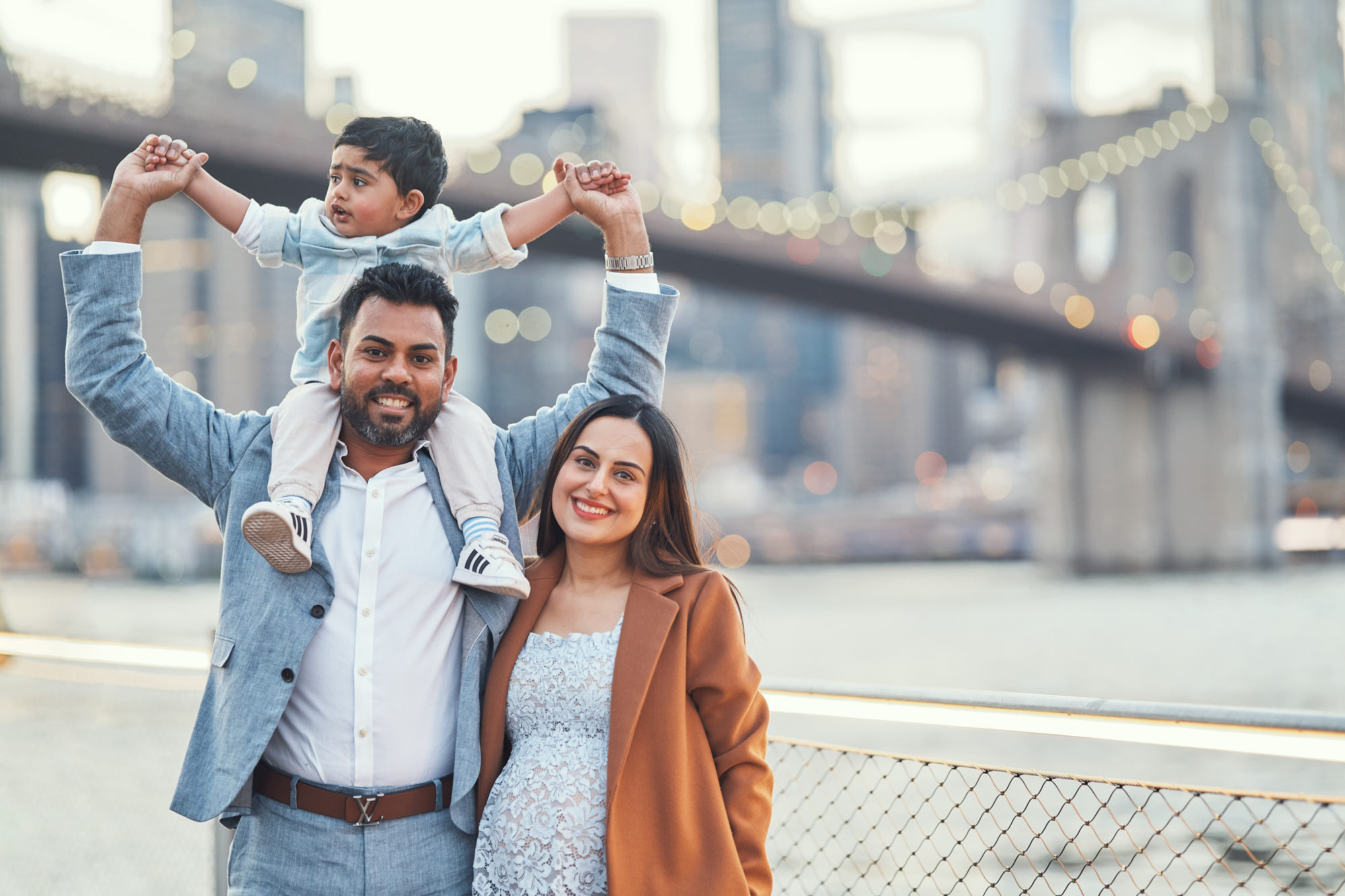 Indian family in traditional dress against the iconic Manhattan skyline and Brooklyn Bridge during sunset at Brooklyn Bridge park