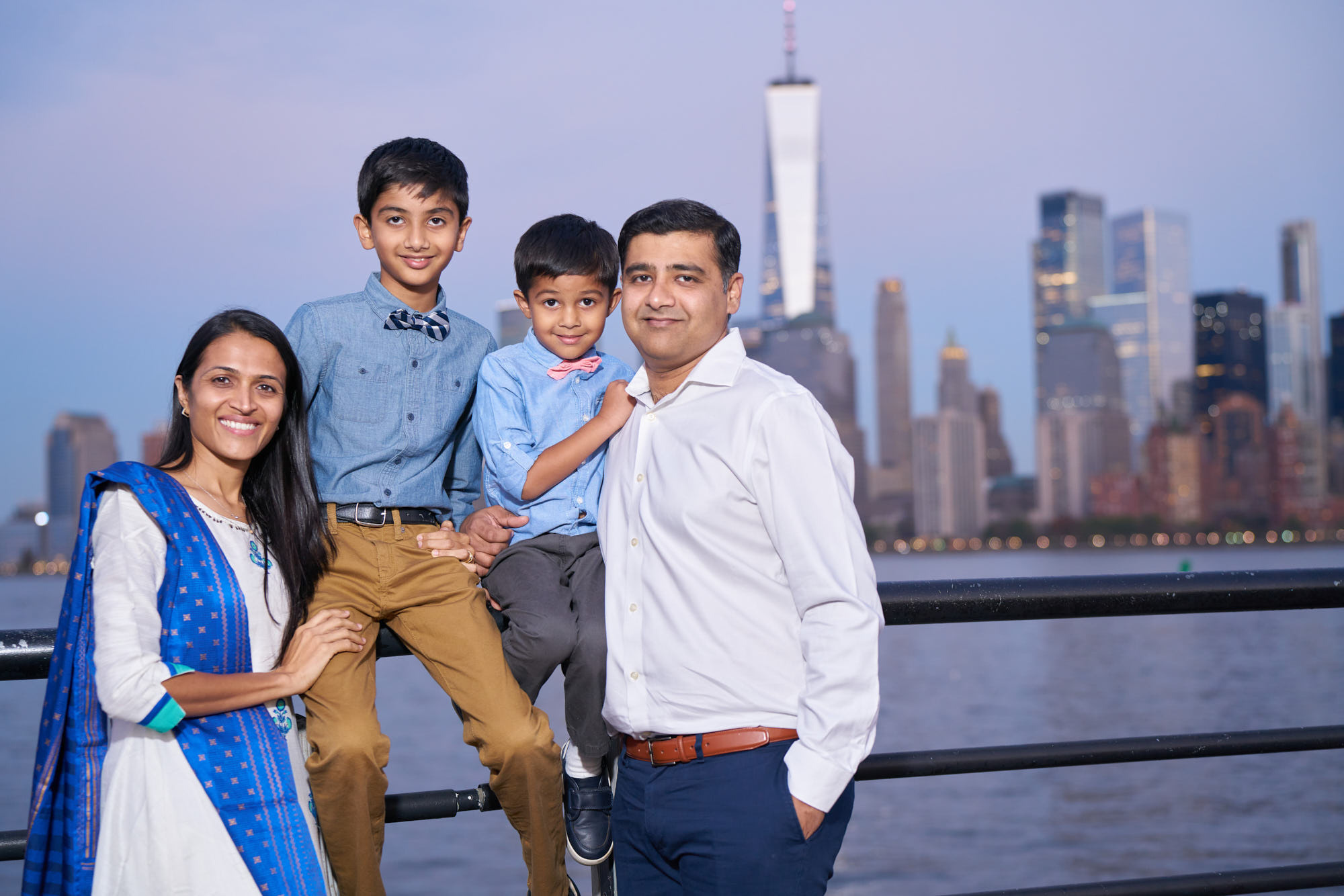 Indian family in traditional dress against the iconic Manhattan skyline during sunset at Liberty State Park, NJ.