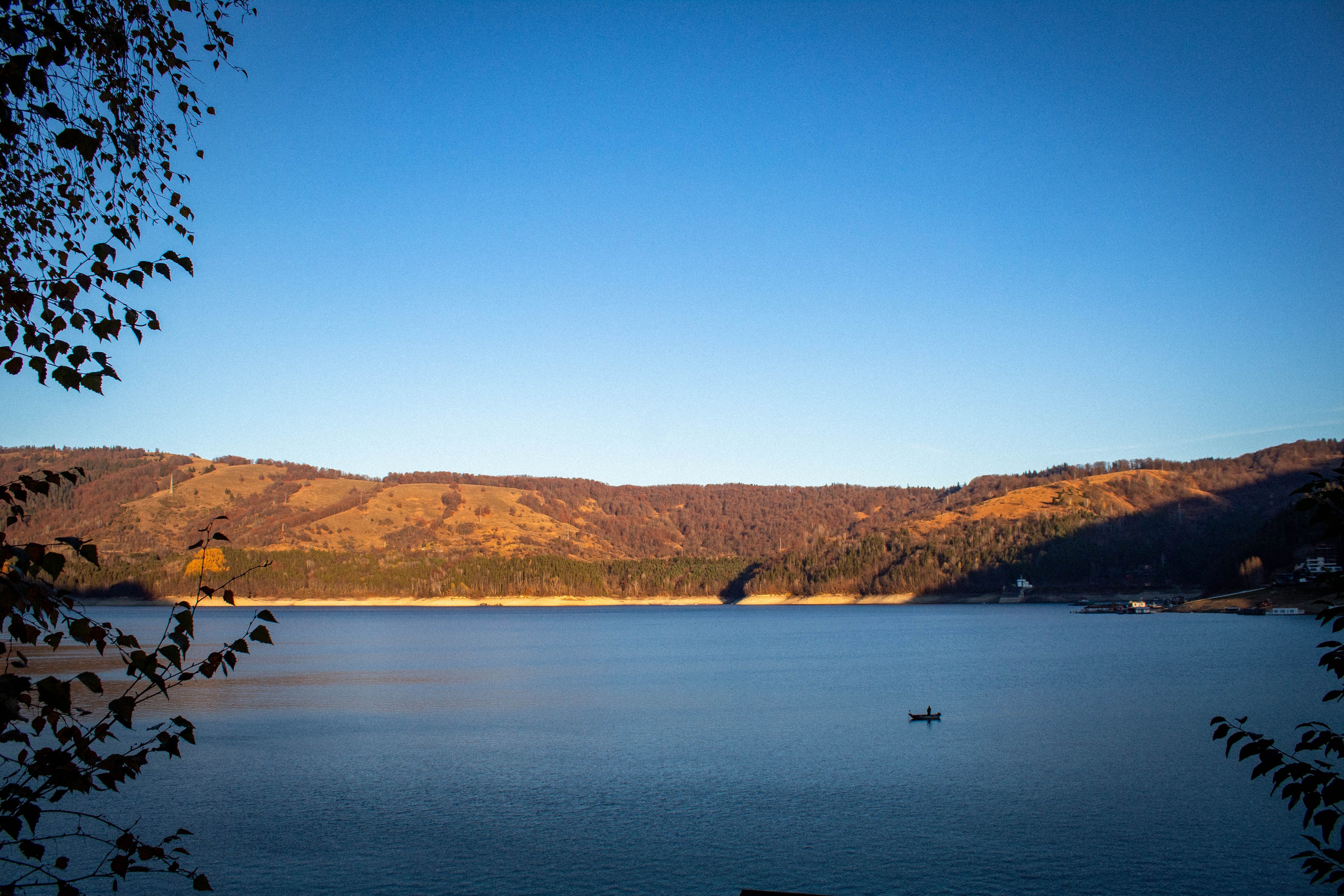Winter lake partially covered in ice with rolling hills under a clear sky.