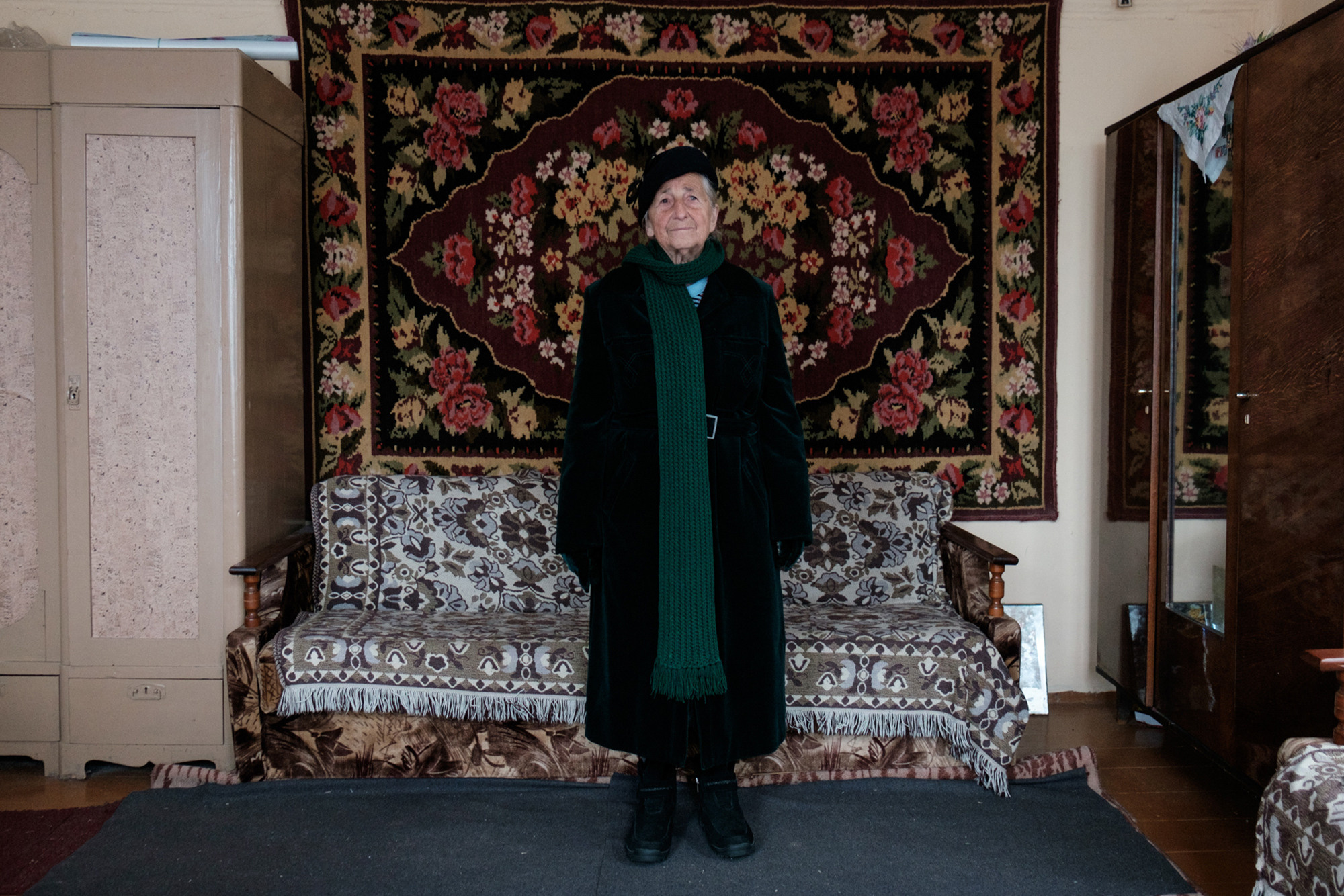 Vera is standing in a black coat and a black hat. She relishes hat, it is her favorite accessory. Before Vera was retired she had been working at the passport office in Volozhyin. Every time she had a business trip to Minsk from Volozhyn Vera bought hats. 