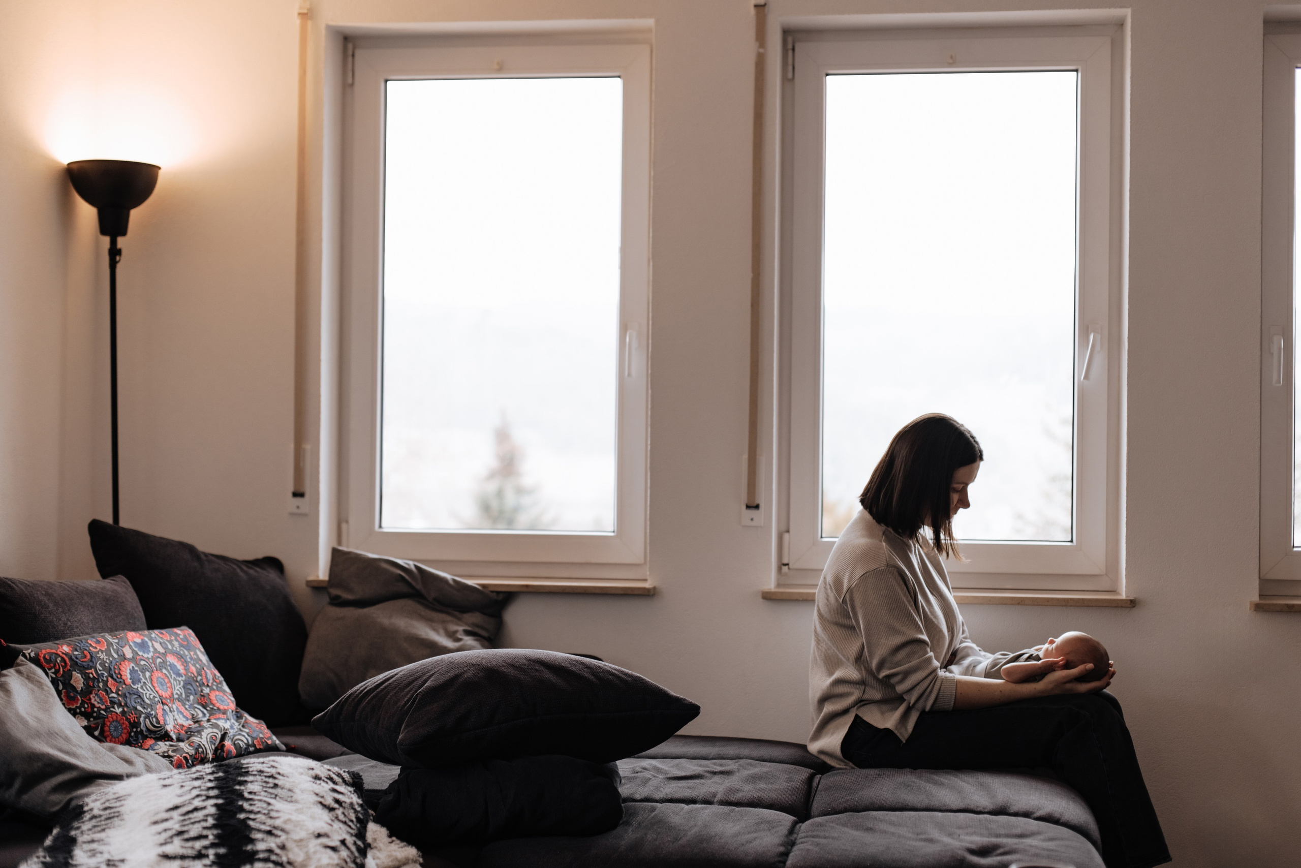 Mutter sitzt am Fenster und hält ihren Sohn im Arm.