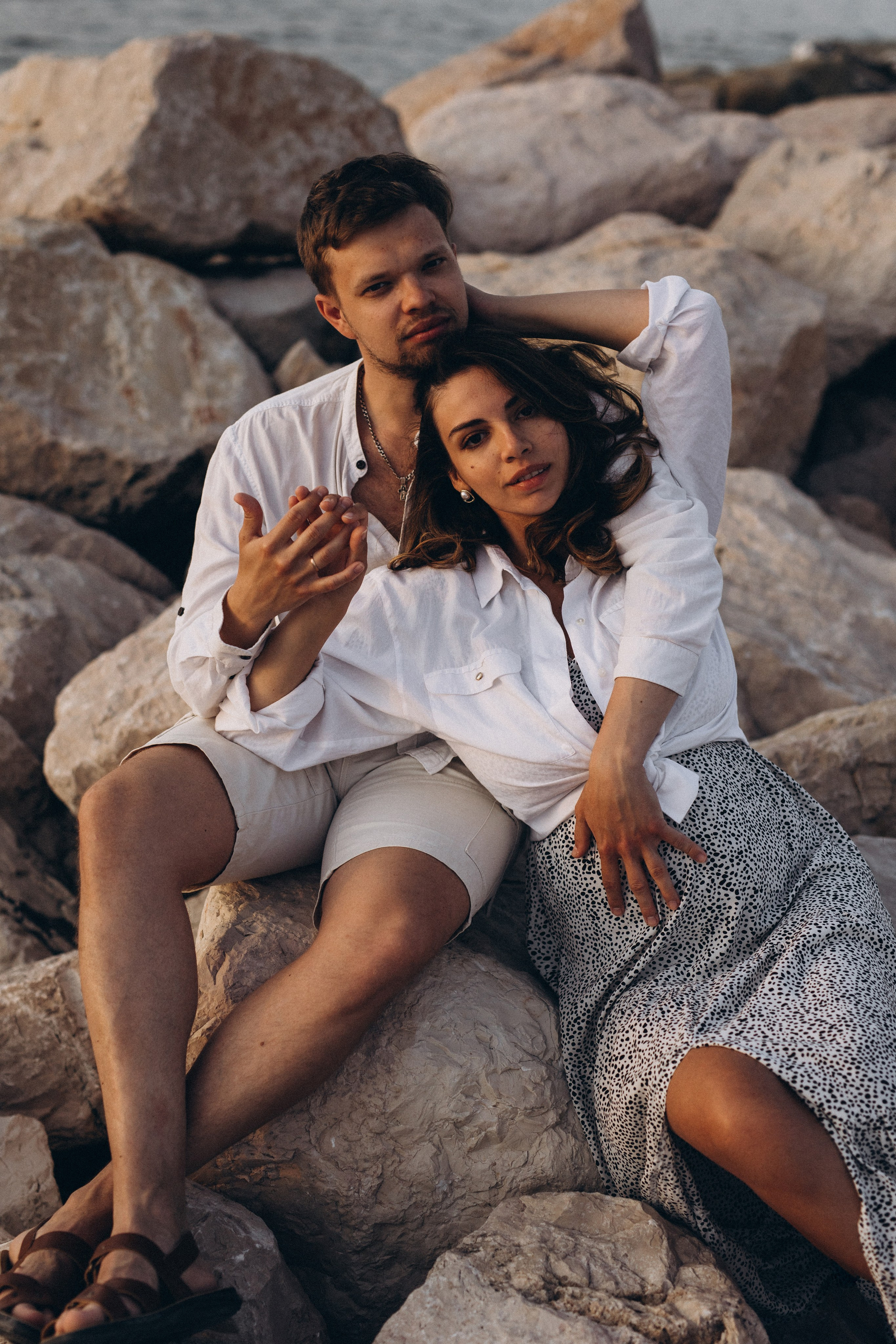 Innamorati seduti sugli scogli vicino al mare in luce naturale