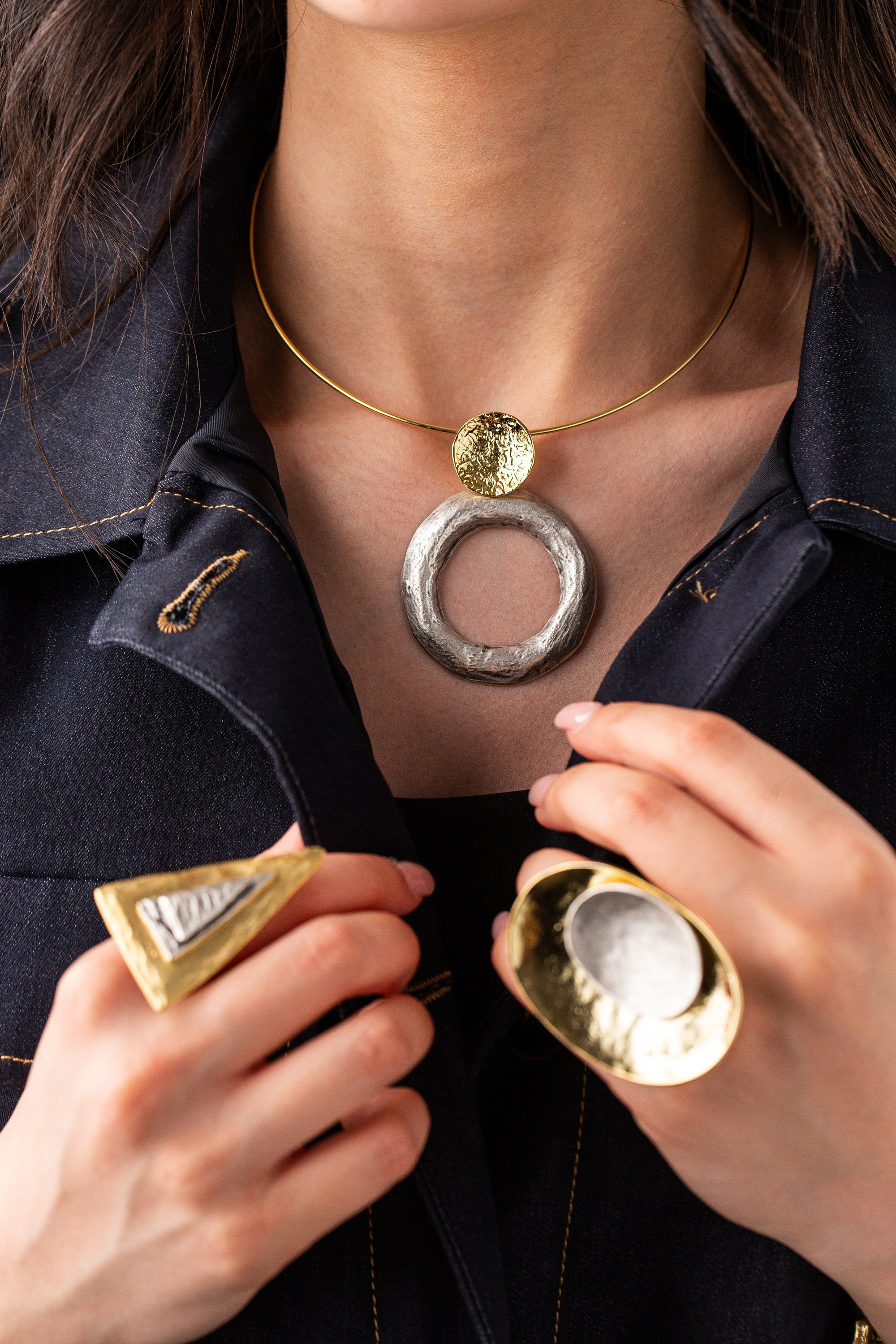 Qızıl və gümüş boyunbağı və abstrakt formalı iki rəngli üzük taxan şəxs.