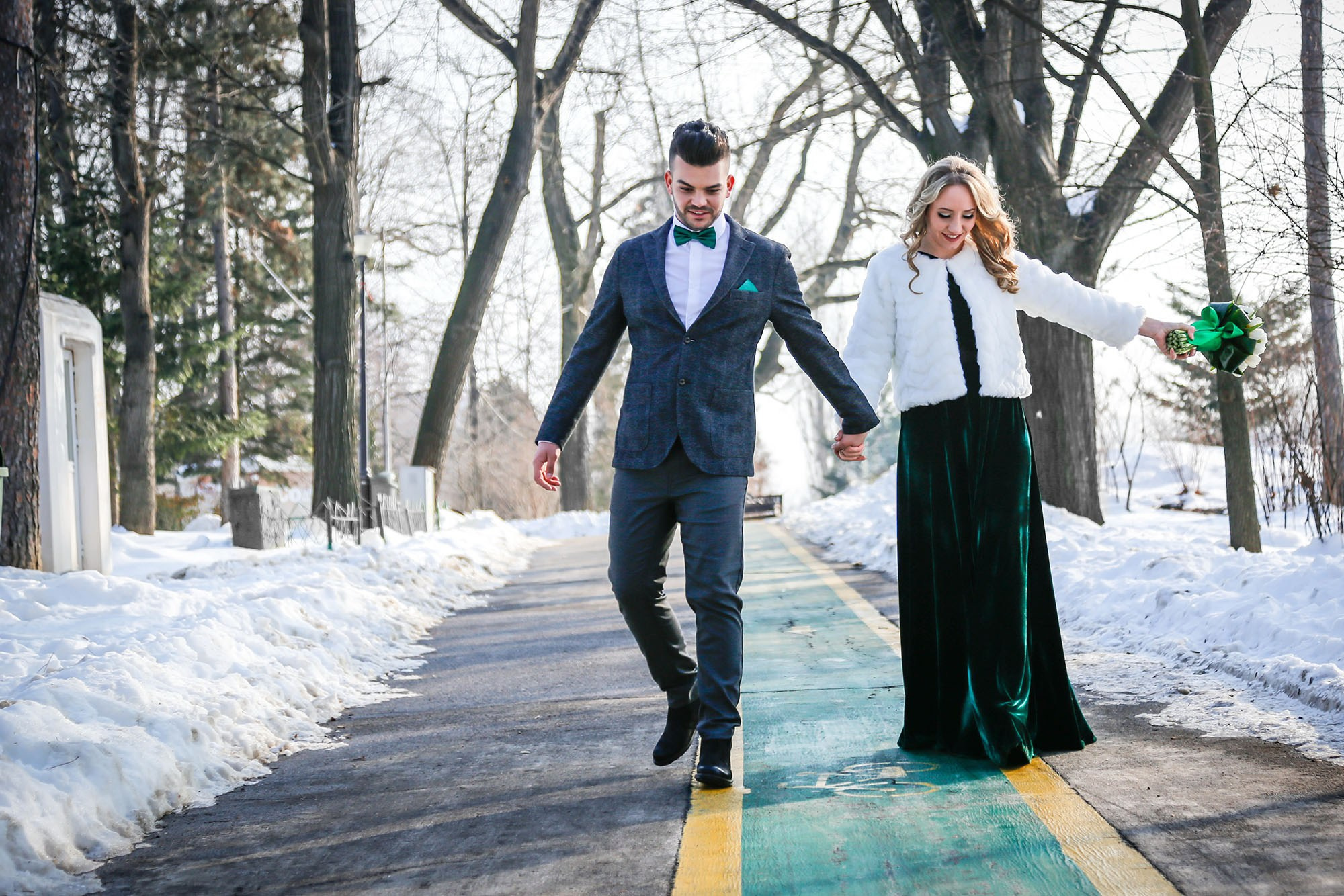Newlyweds walking hand in hand through the snow toward the camera, smiling happily during their winter wedding photo shoot.