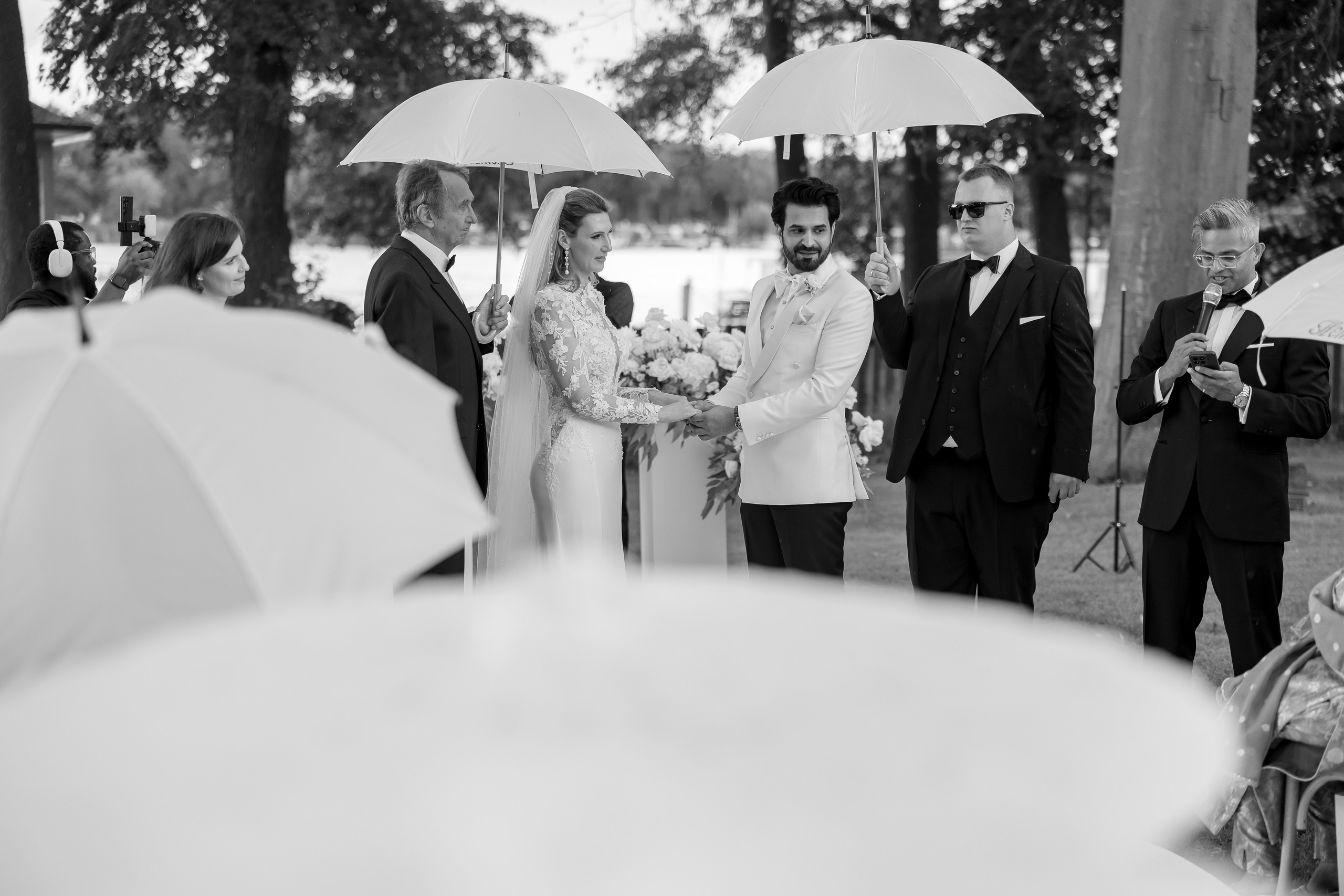 Hochzeitsgäste mit Regenschirmen am See – Schwarz-Weiß-Foto an der Remise am See