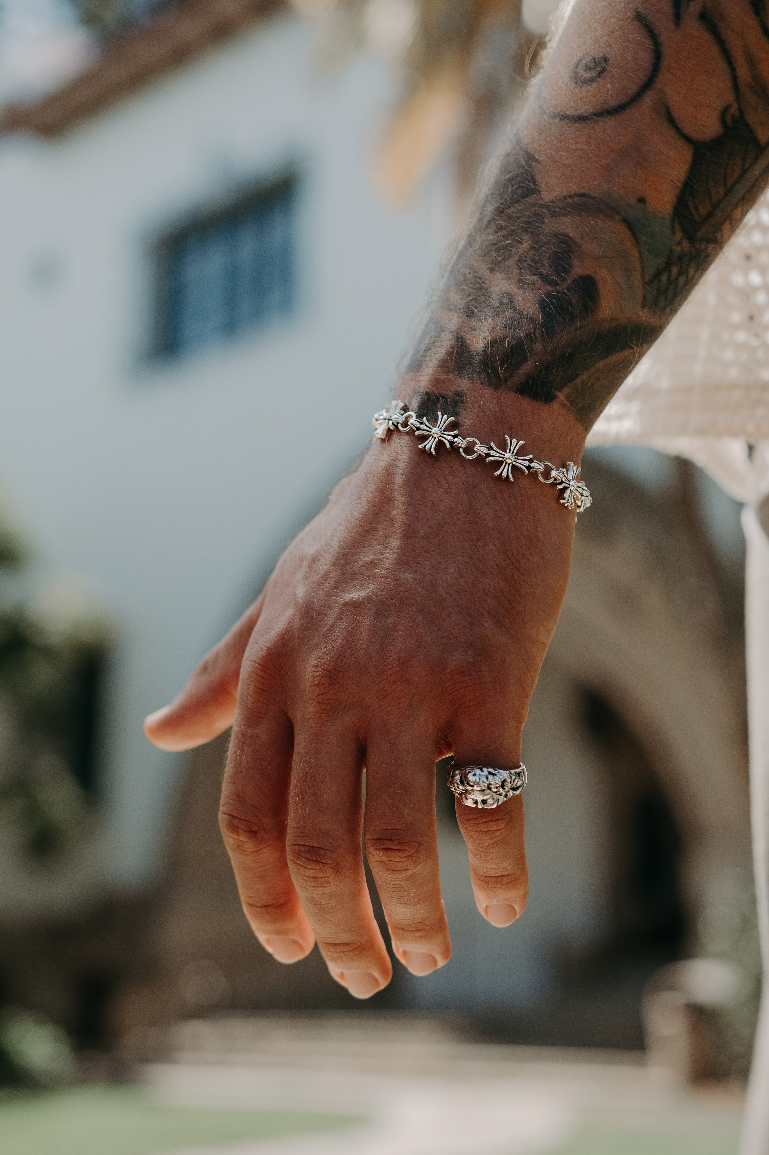 Tattooed model holding a silver pendant necklace, blending masculinity and elegance.