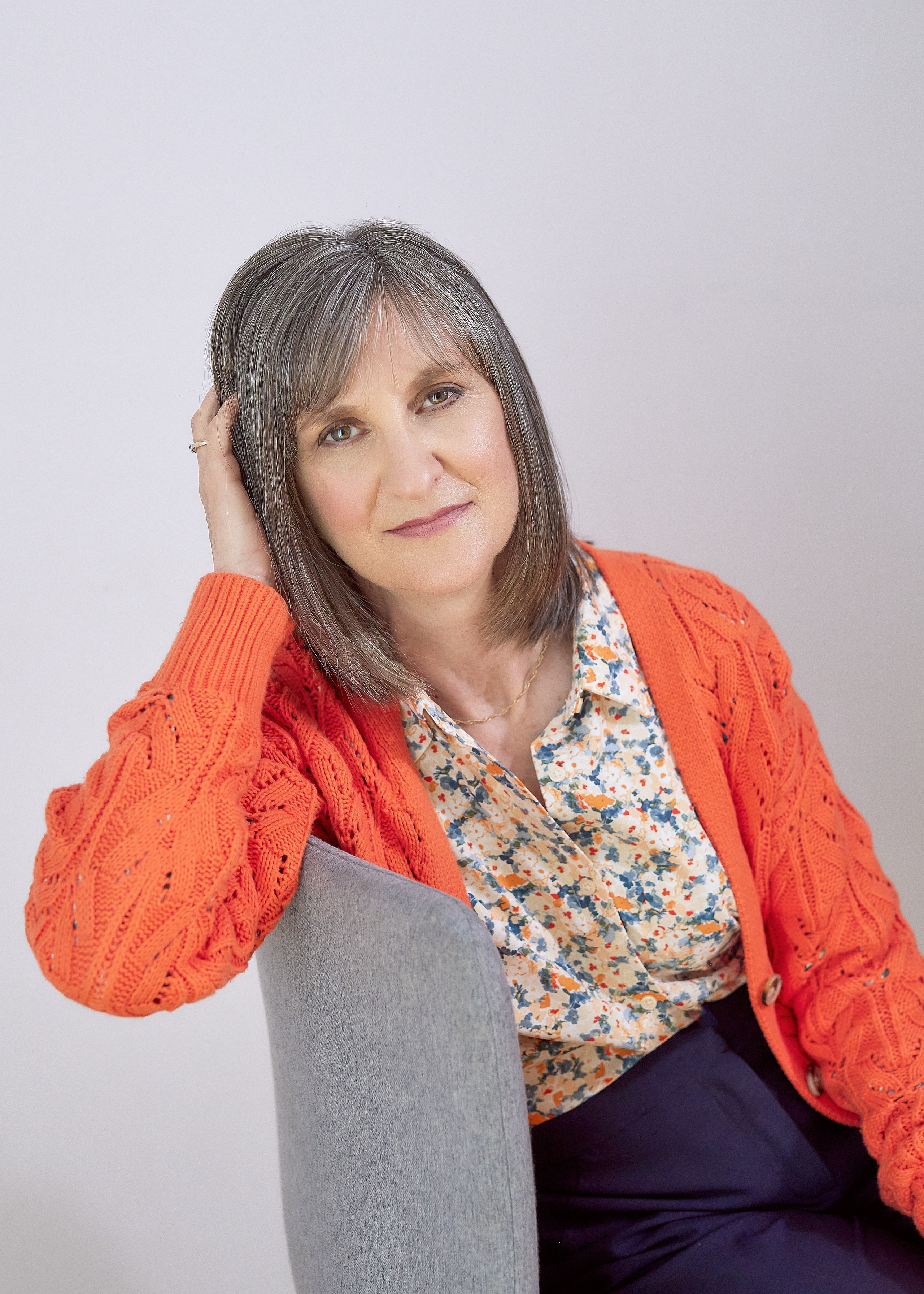 woman with grey hair and orange cardigan leaning on back of chair 