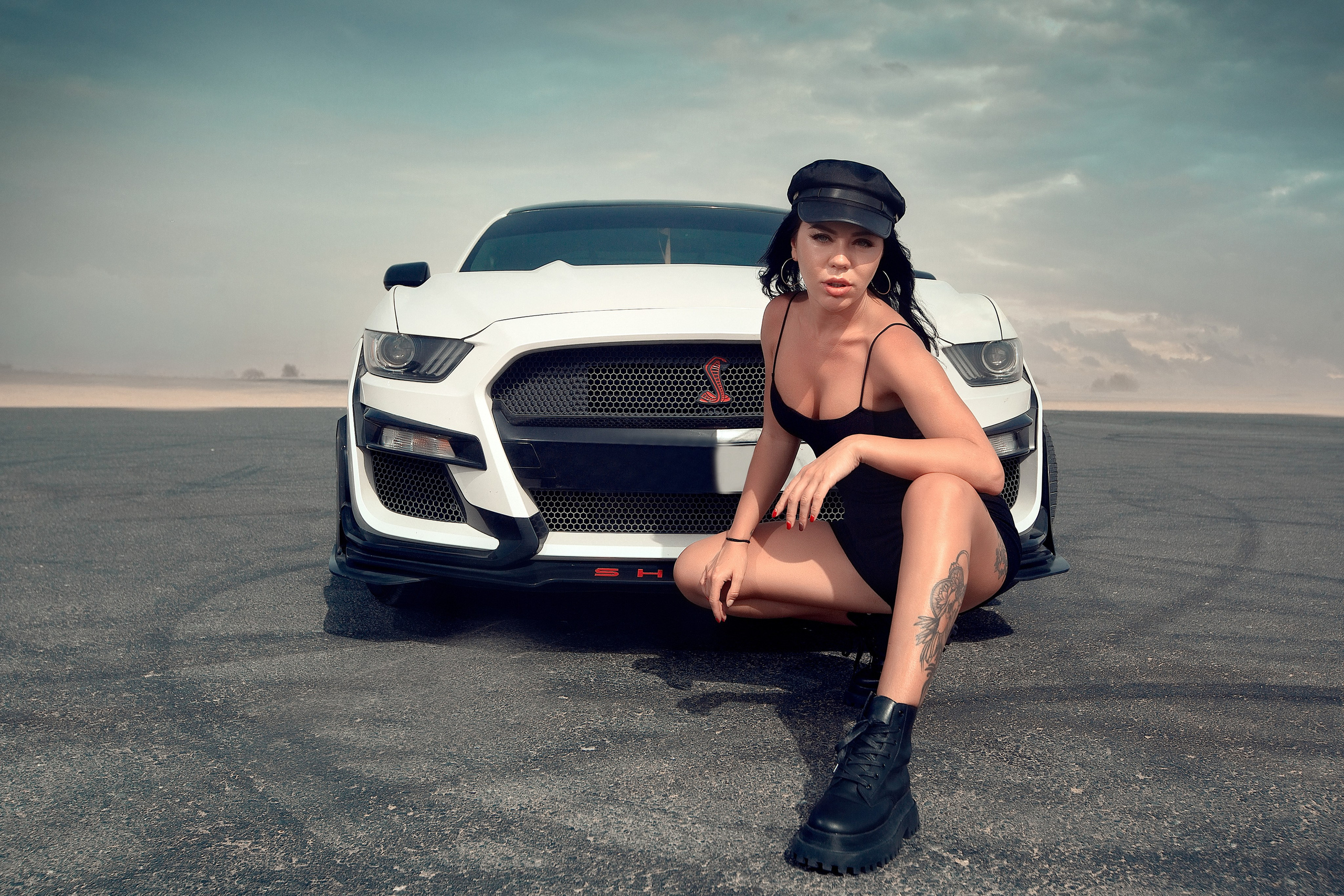 A girl in a black cap sits next to an exclusive, beautiful car against the backdrop of Dubai’s sandy roads